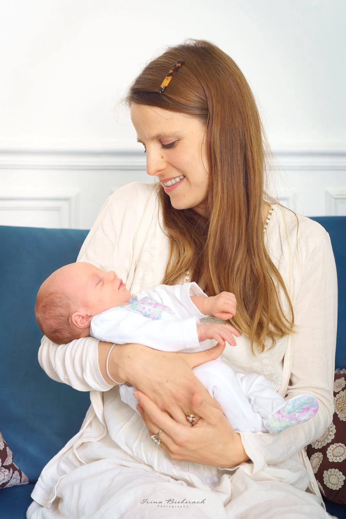 Maman regarde son bébé dormir assise sur un canapé bleu dans un salon