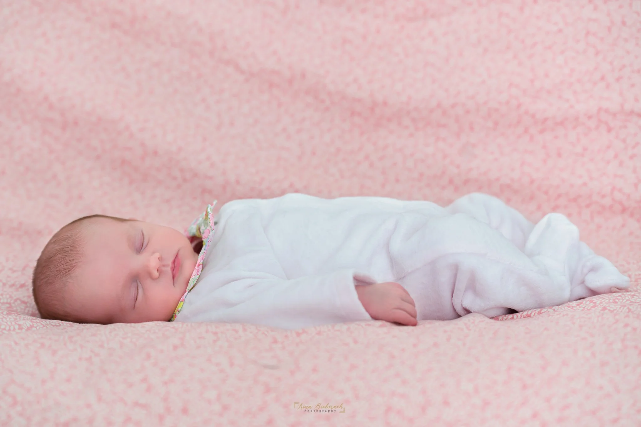 Bébé fille en body rose dort sur une couverture rose aux motifs légèrement fleuris
