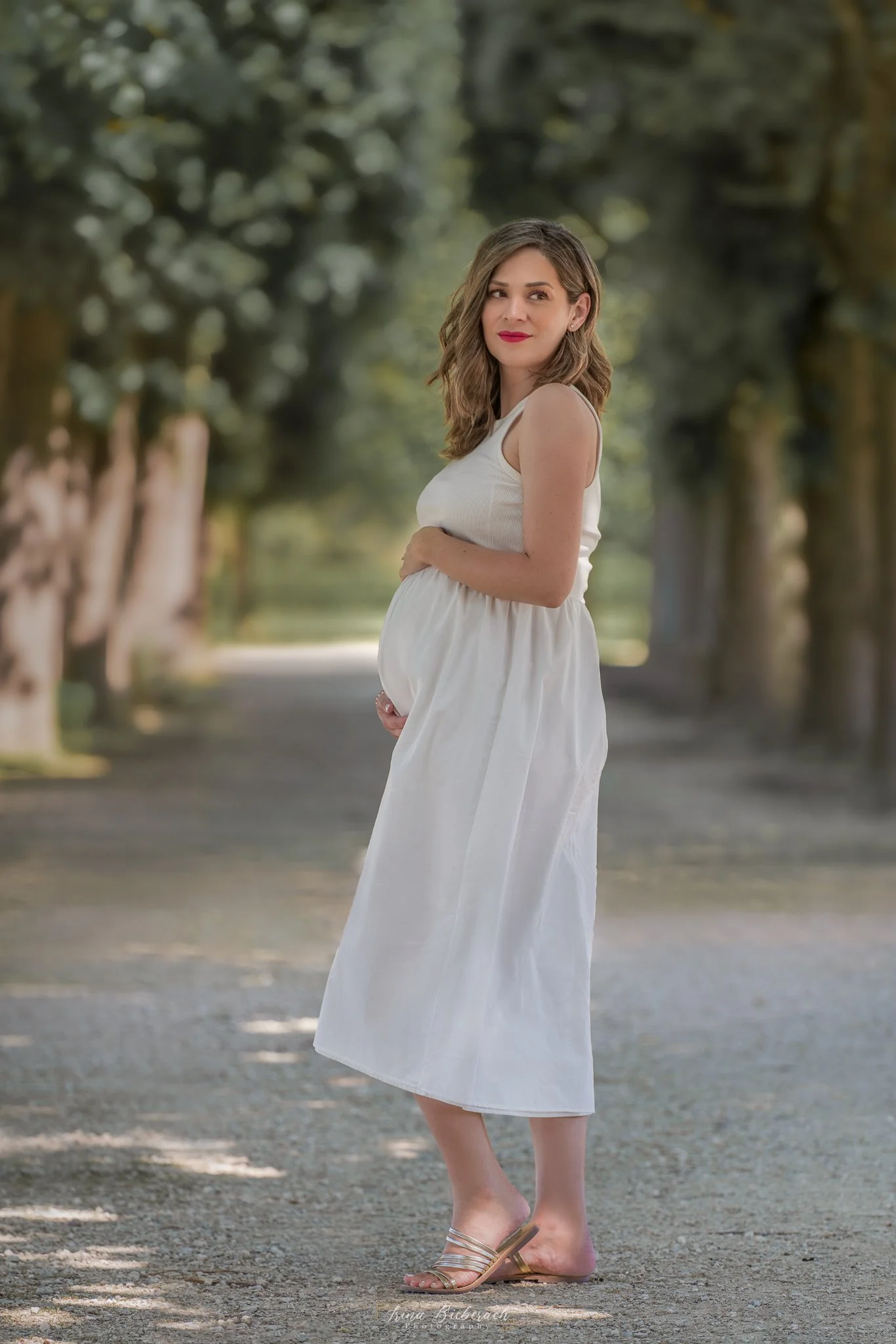Femme enceinte en robe blanche pose devant une allée des arbres du jardin du château de Saint Germain en Laye