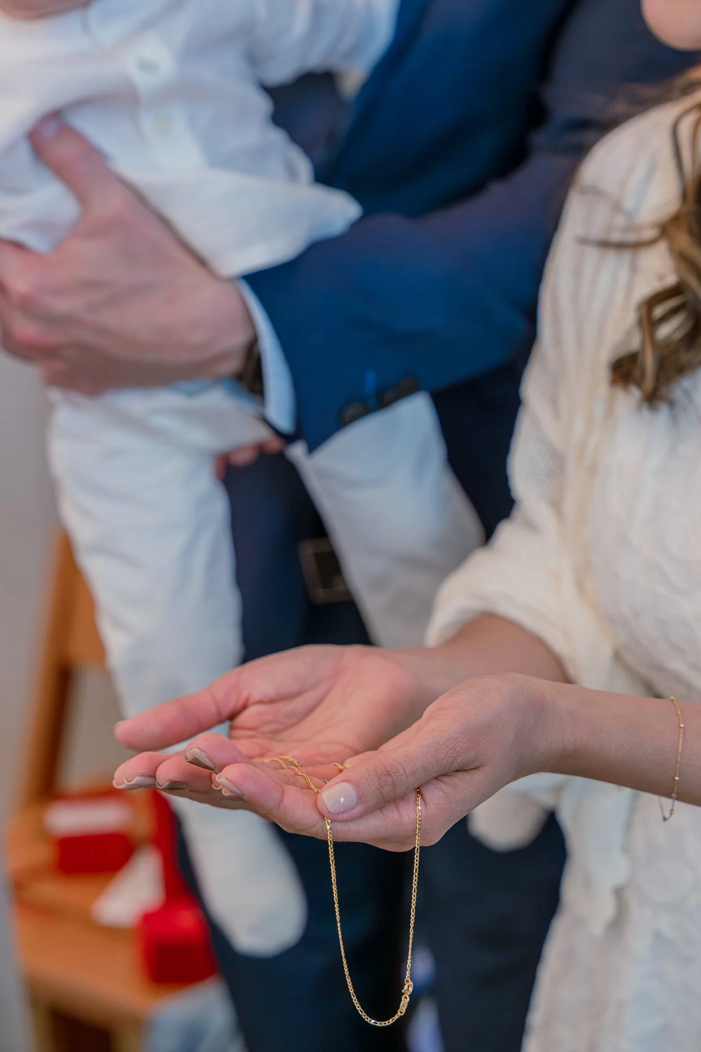 Mains d'une maman tiennent une chaine d'or lors d'un baptême à Paris