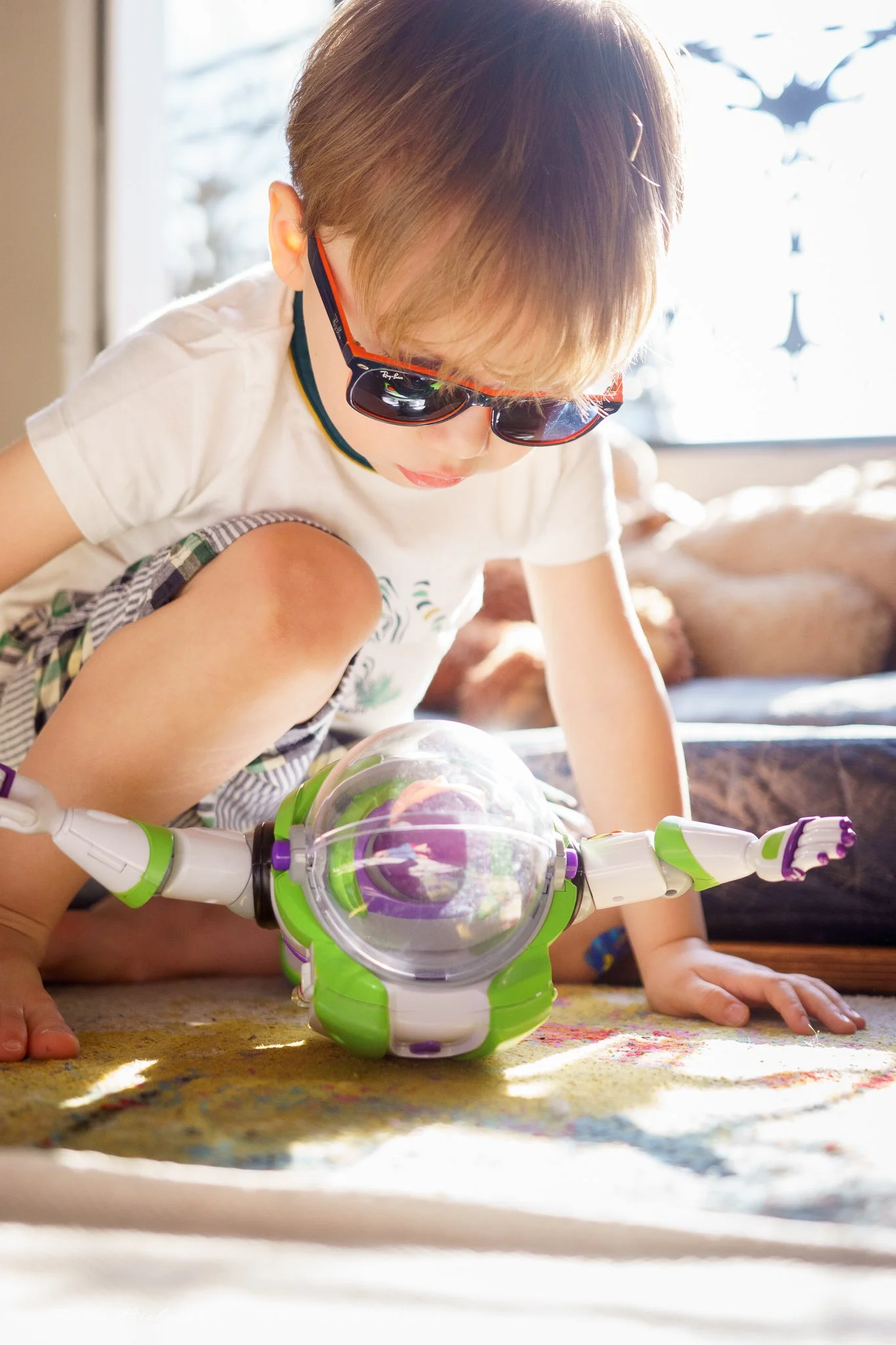Petit garçon assis devant une fenêtre ensoleillée porte des lunettes et regarde son jouet Buzz l’éclair 