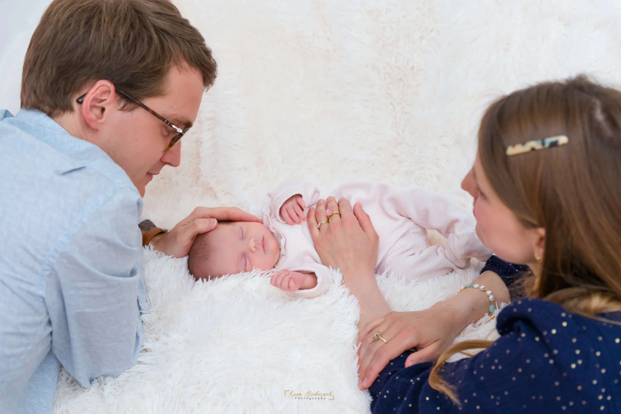 Maman et papa regardent leur fille nourrisson dormir sur une couverture posée sur un canapé et mettent ses mains sur elle pour l'apaiser lors de son sommeil