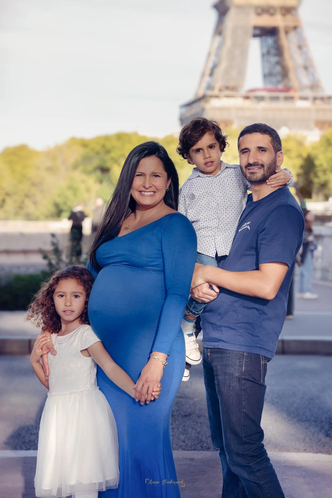 Femme enceinte avec ses deux enfants et son mari posent devant la tour Eiffel