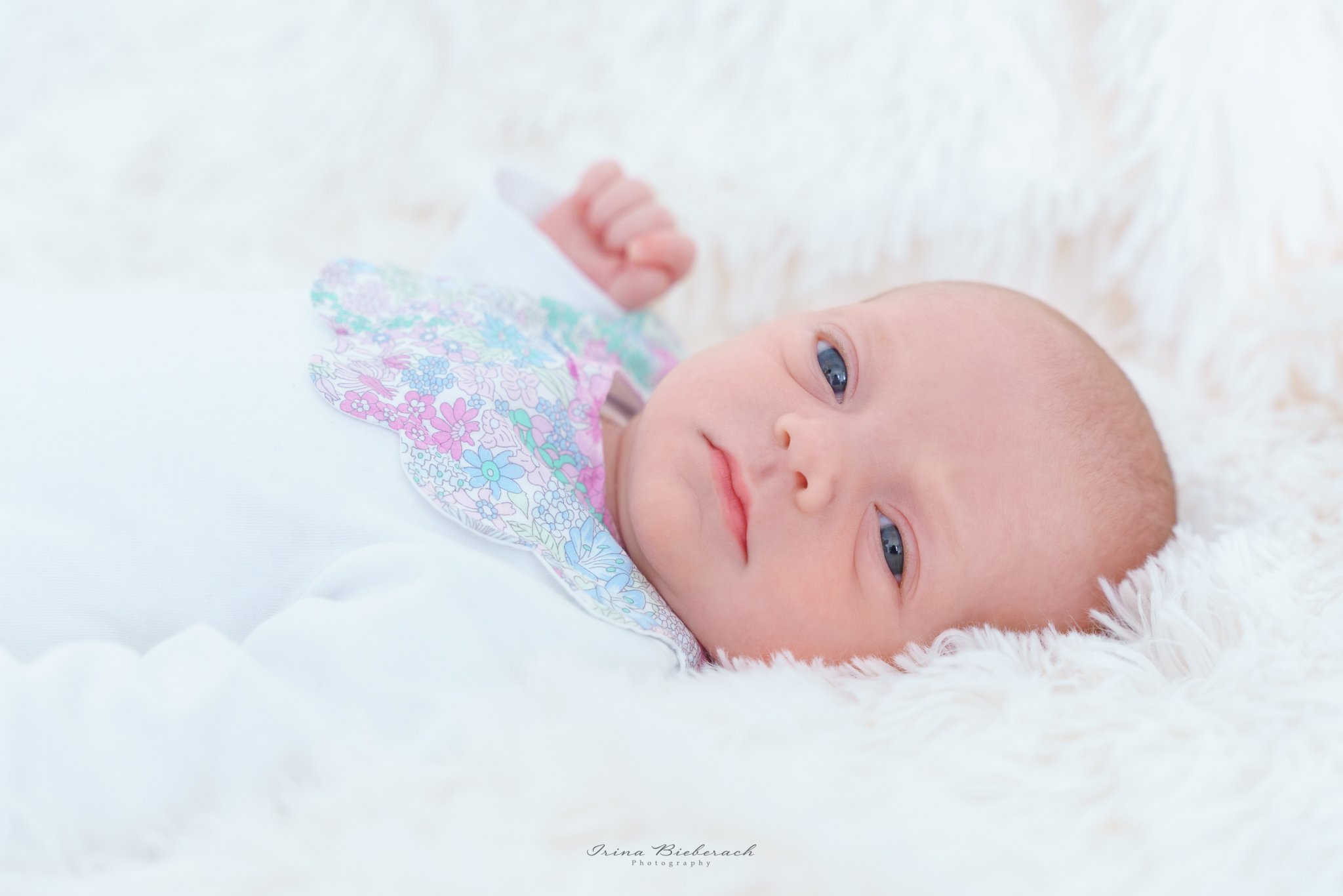 Bébé nouveau-né sur une couverture douce blanche regarde devant 