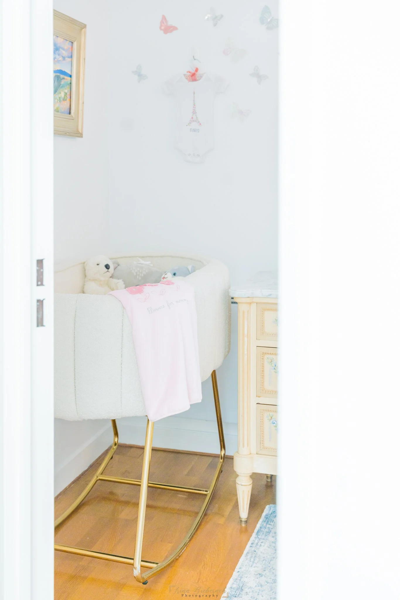 Lit de bébé blanc vu a travers une port entre-ouverte avec un habille rose de bébé sur le bord du lit