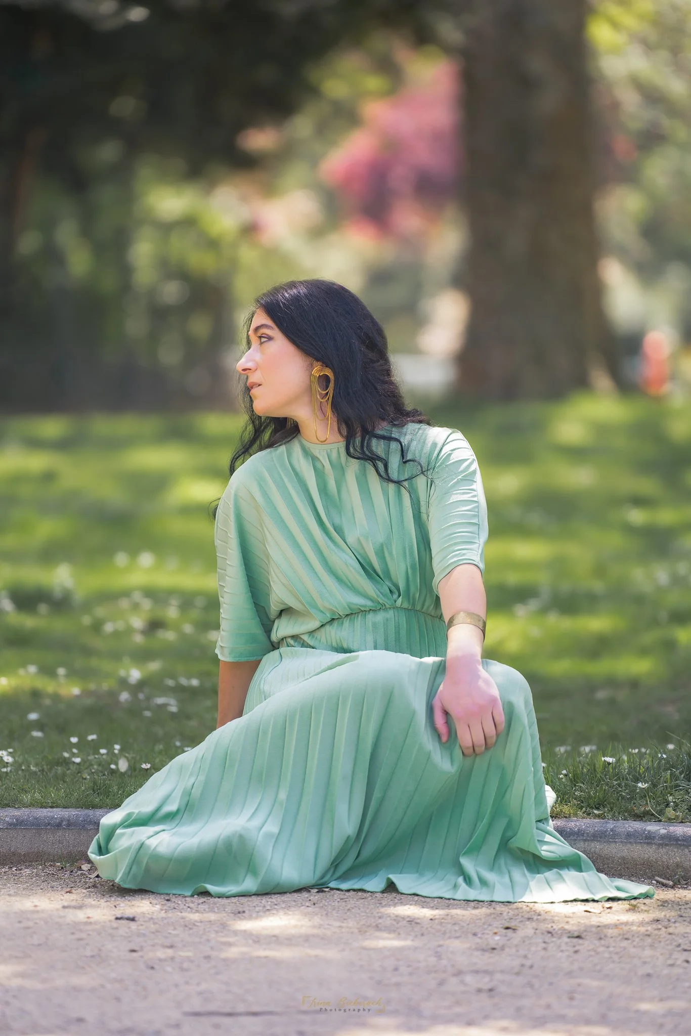 Femme en robe verte fluide assise dans l'herbe d'un parc parisien. Séance bien-être et confiance en soi.