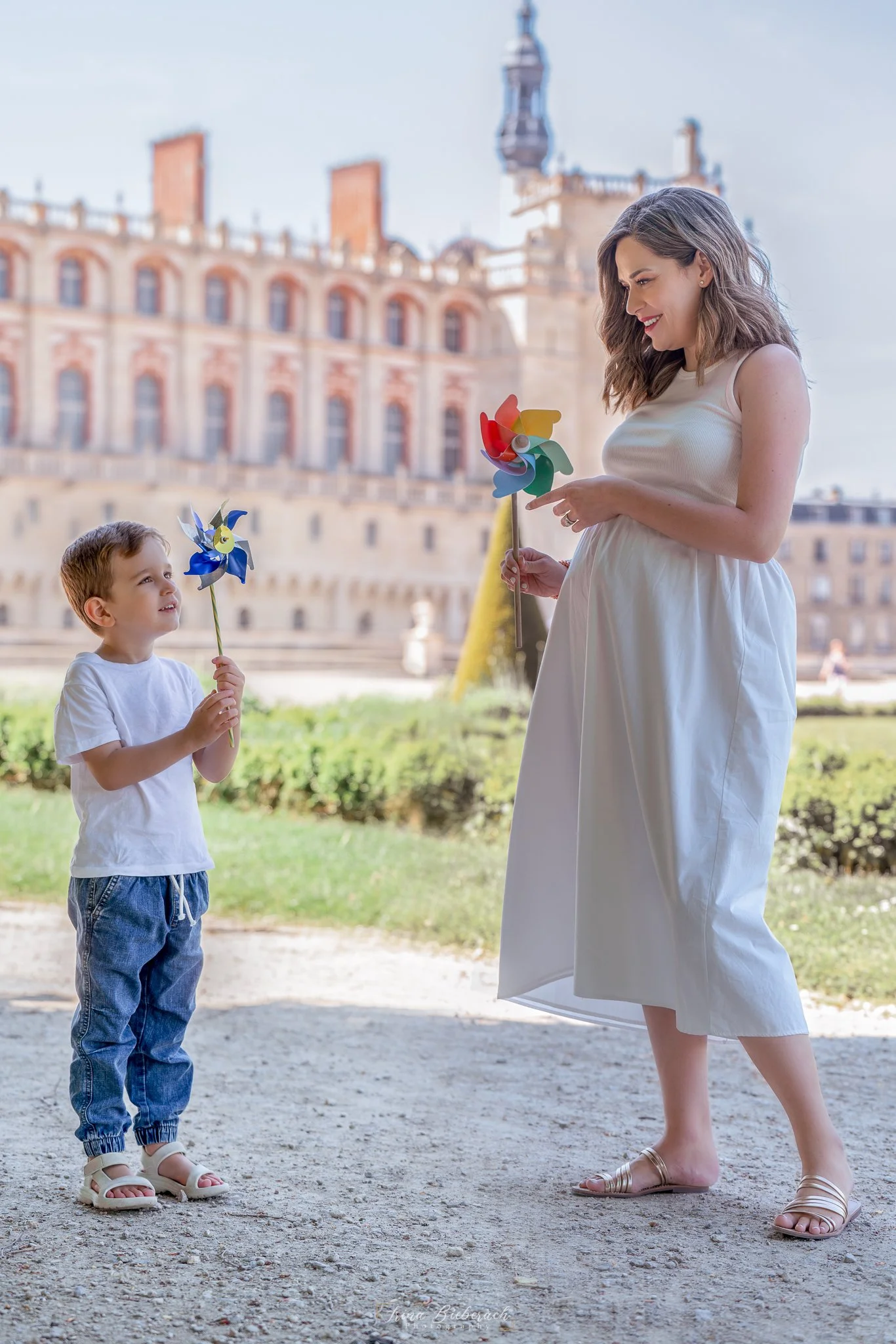 Femme enceinte habillée en blanc joue avec un moulin à vent colorée et regarde son fils dans les jardins du château de Saint Germain en Laye 