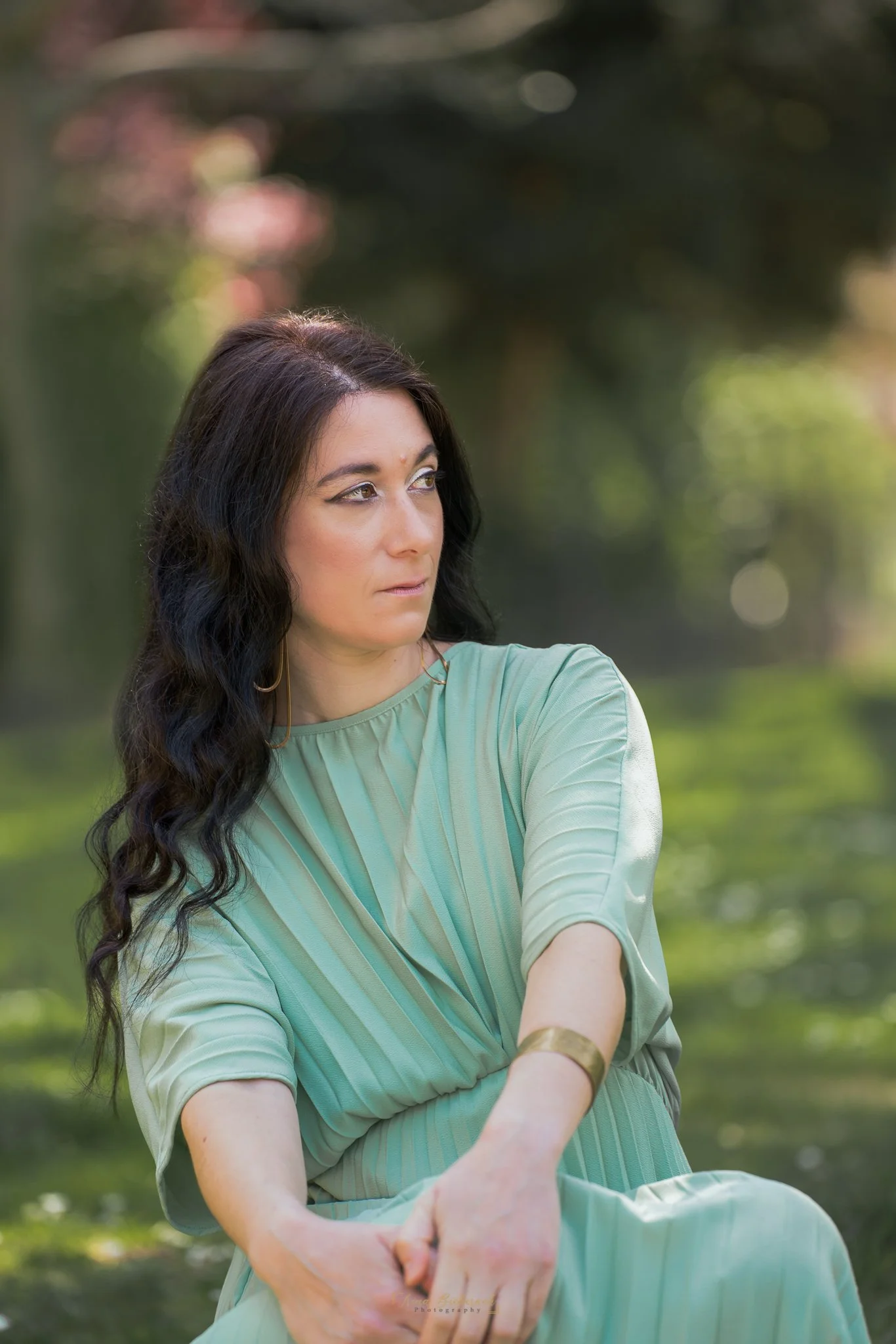 Femme habillée à la chevelure longue brune et élégamment habillée en en vert assise dans un jardin parisien 