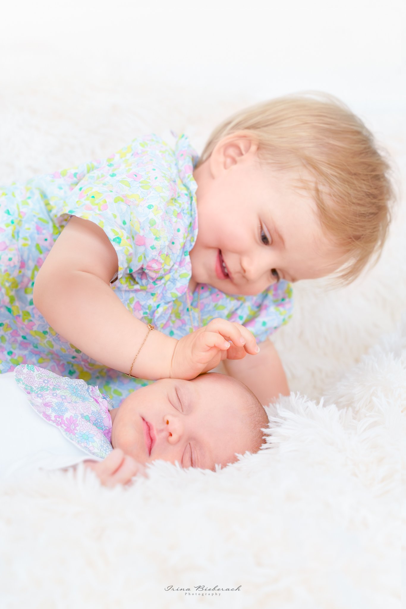 Petite fille souriante touche le visage de sa soeur bébé qui dort sur une couverture blance