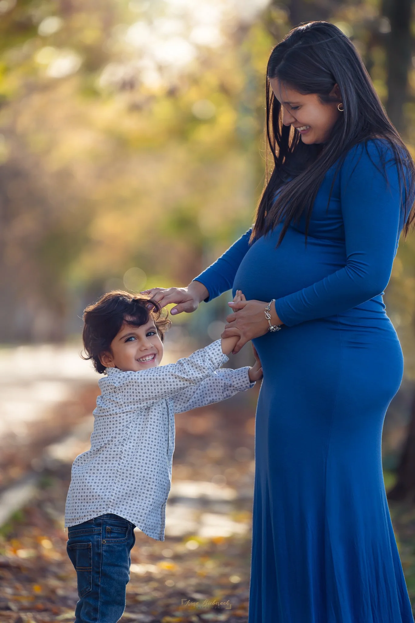 Femme enceinte regarde son petit fils garçon qui sourit et touche le ventre rond de sa maman pendant un coucher de soleil d'automne dans l’allée des Cygnes à Paris