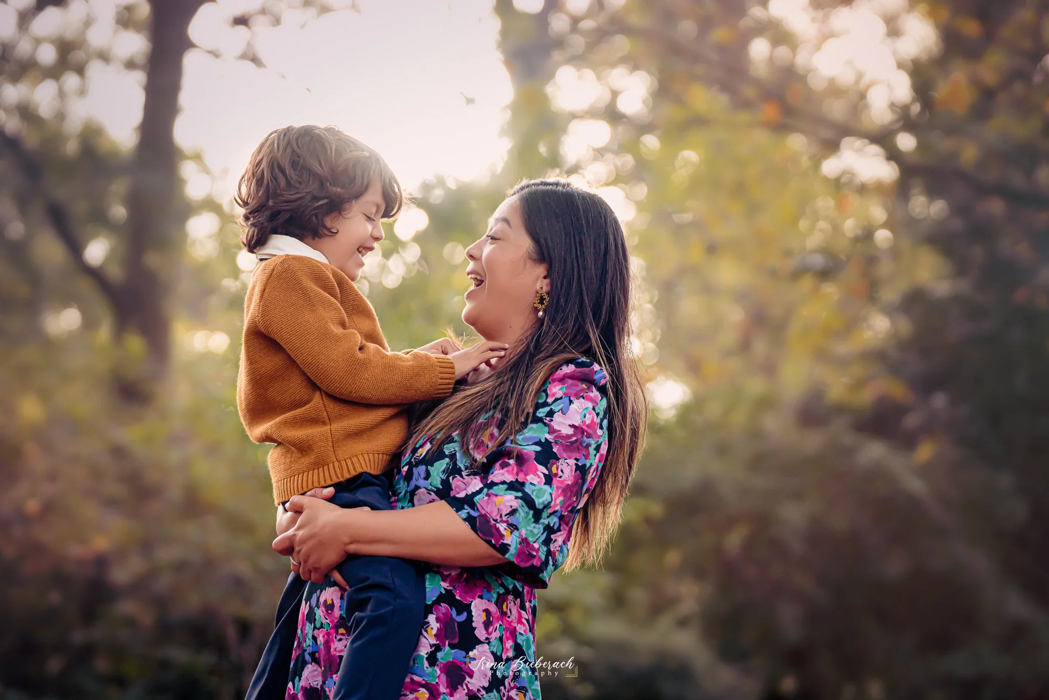 Femme brune porte son fils dans les bras et rie avec luis dans  le parc Montsouris pendant un après-midi d'automne
