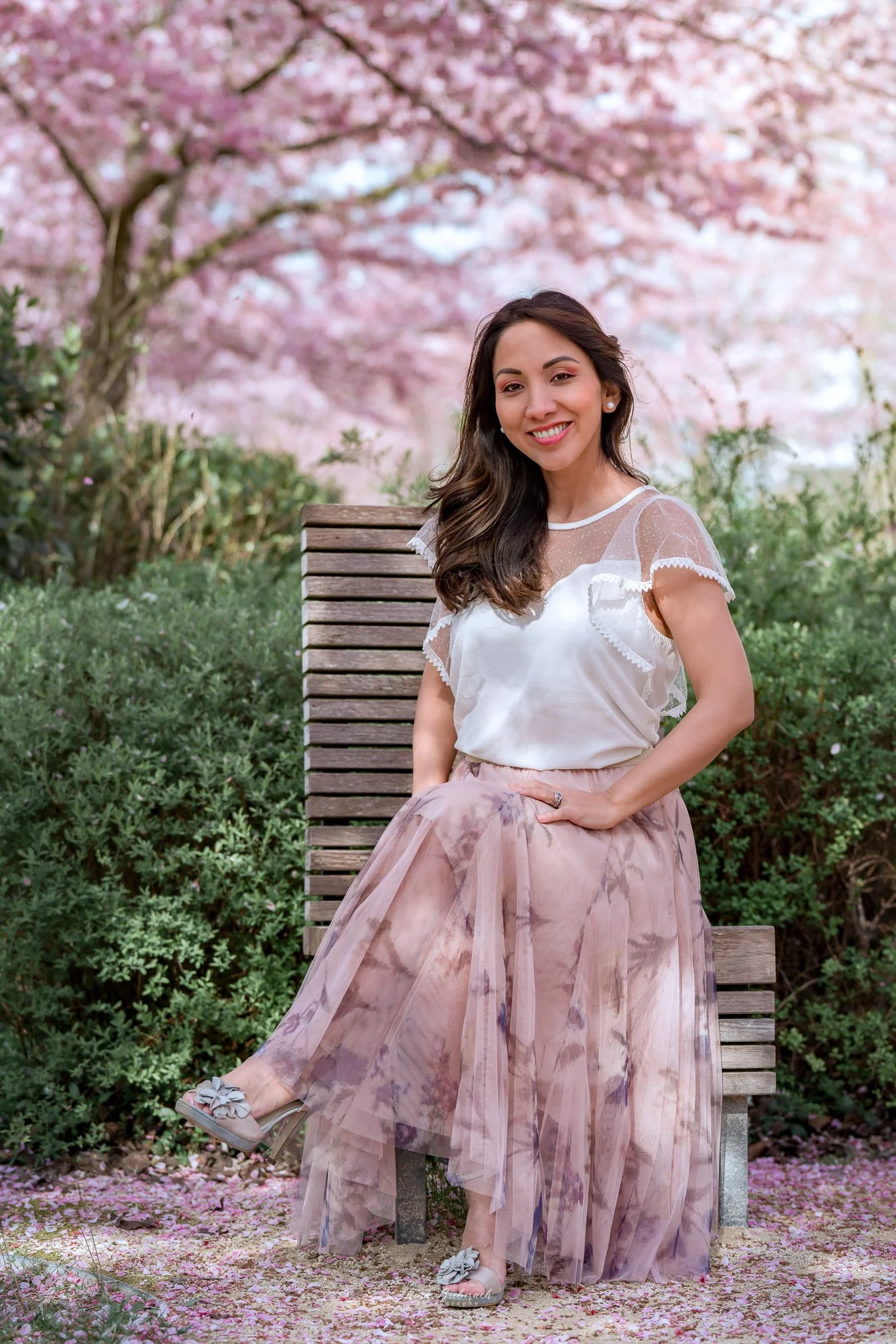Jeune femme assise de façon élégante dans un parc de Paris  sourit, avec les cerisiers sakura au fond
