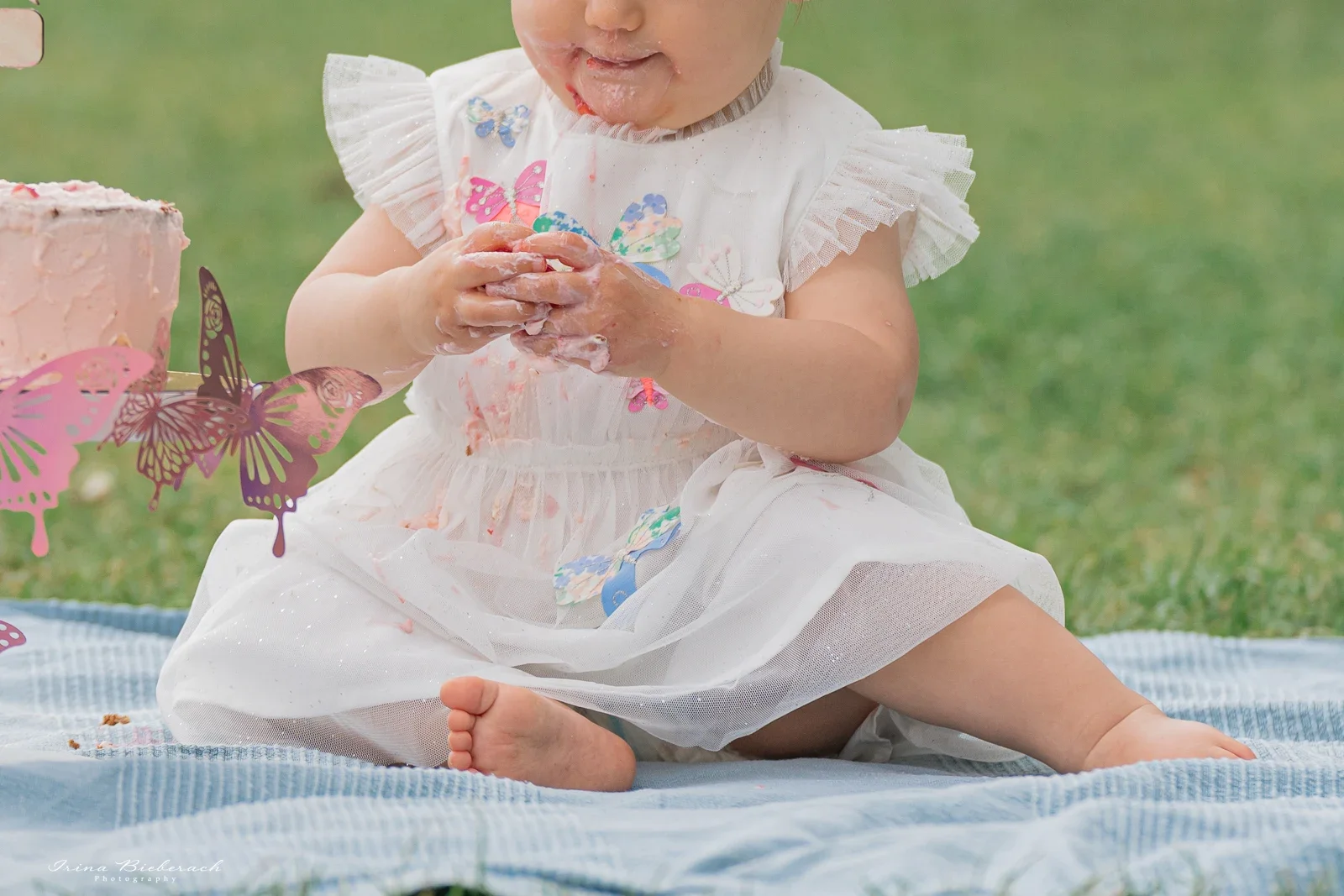 Gros plan d'un bébé assis au Trocadéro, souriant avec les mains pleines de gâteau rose après sa séance photo 1 an.