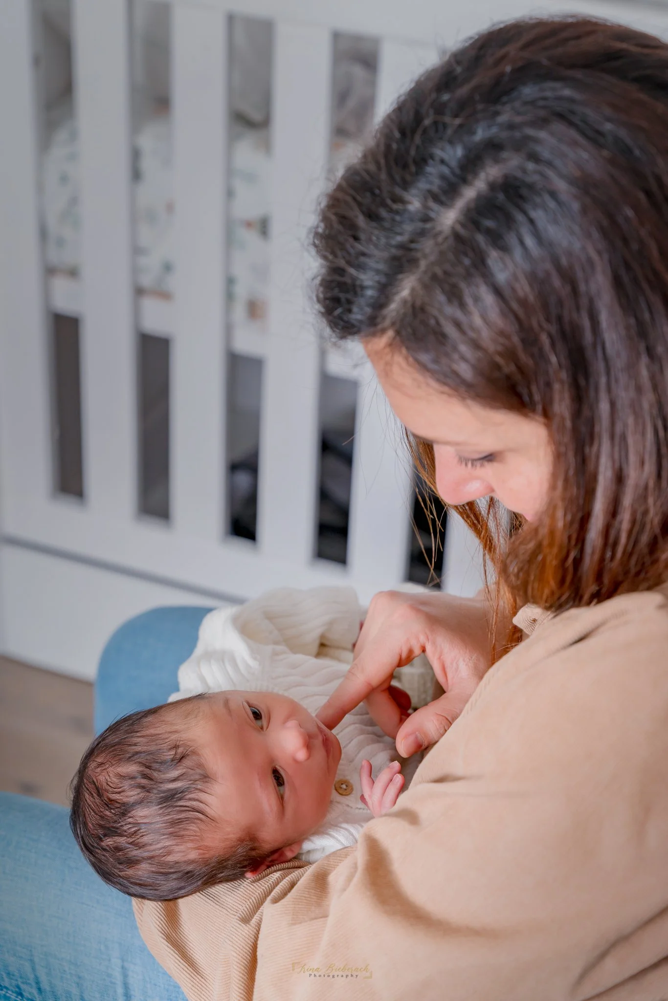 Jeune femme touche la bouche de son garçon nouveau-né assisse dans la chambre du bébé et à côté du lit de bébé 