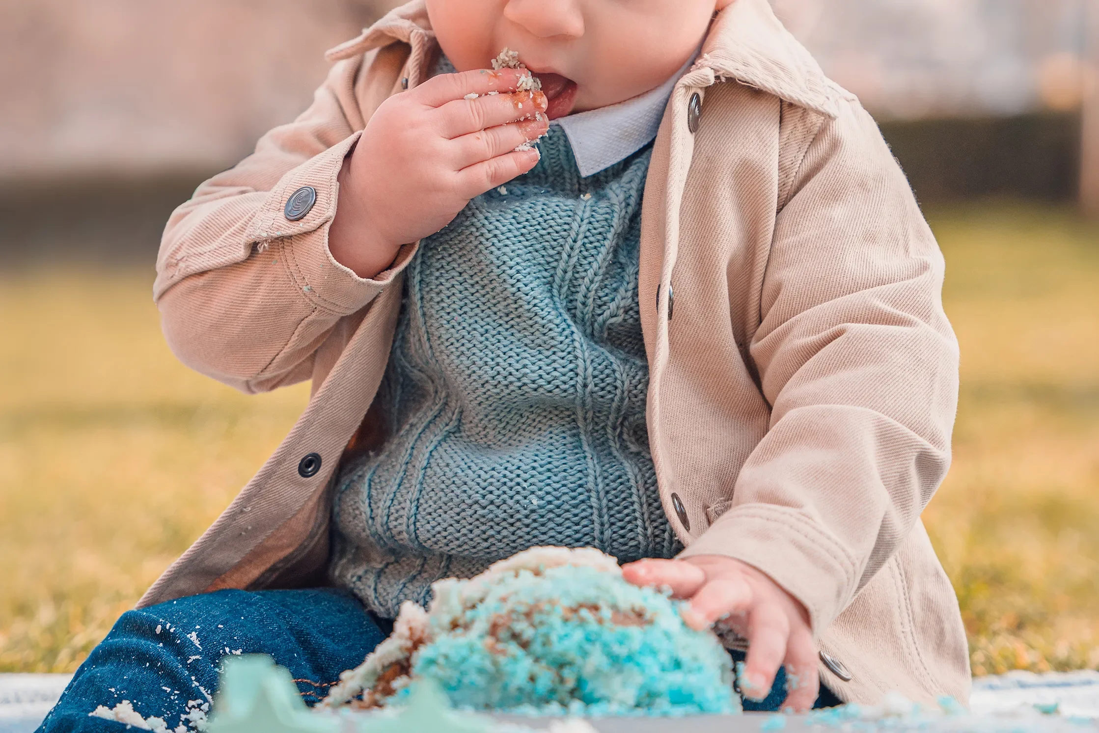 Détail des mains d'un enfant de 1 an manipulant un gâteau d'anniversaire bleu en extérieur.