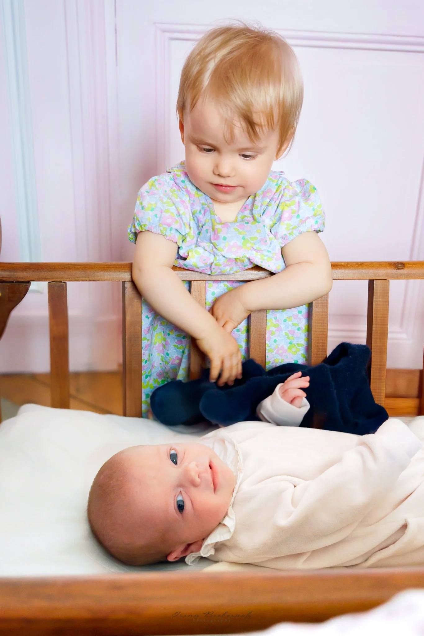 Bébé fille dans son lit en bois de bébé regarde devant pendant que sa soeur la regarde