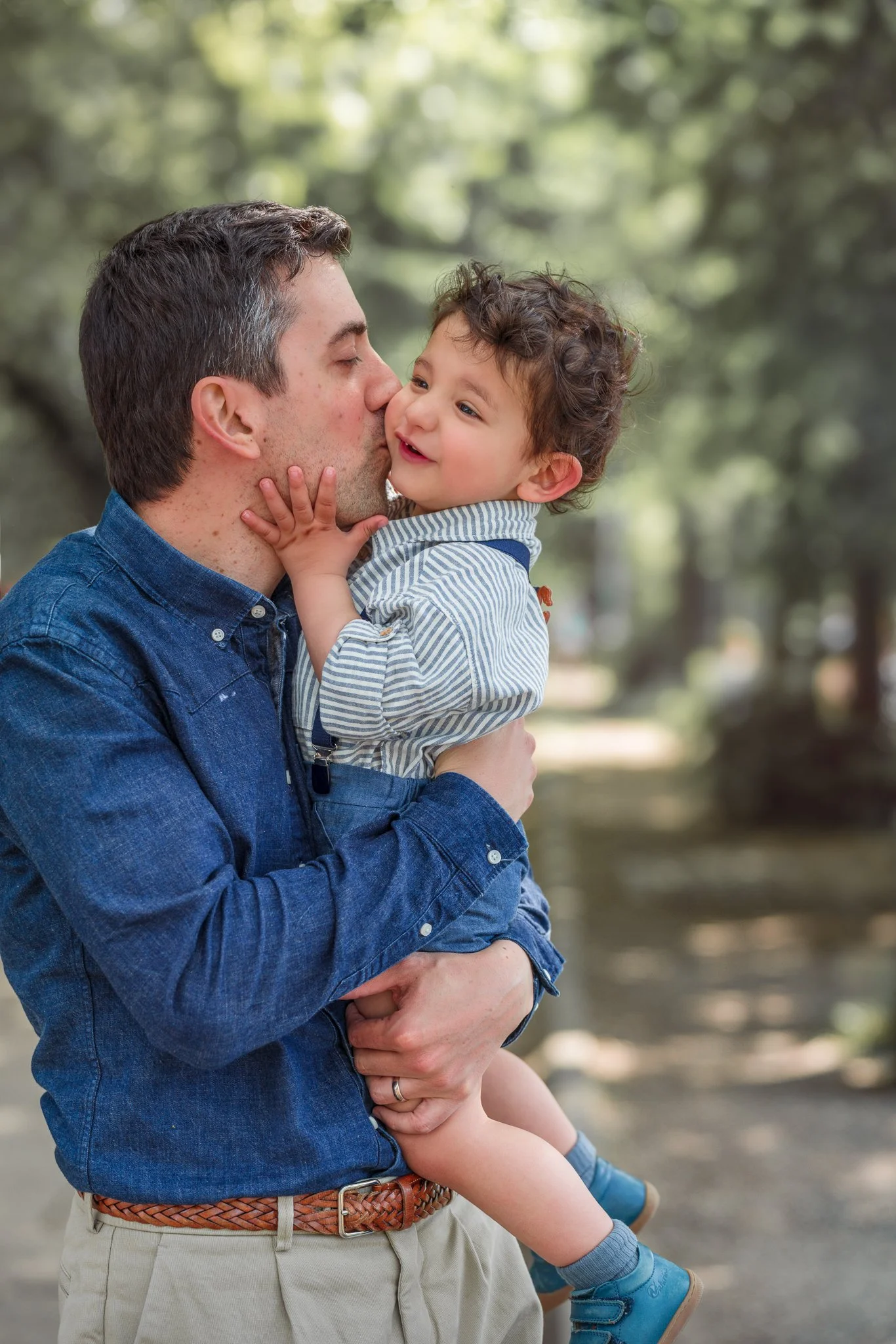 Papa élégant embrasse son petit fils qui porte dans les bras dans l’allée des Cygnes à Paris 16