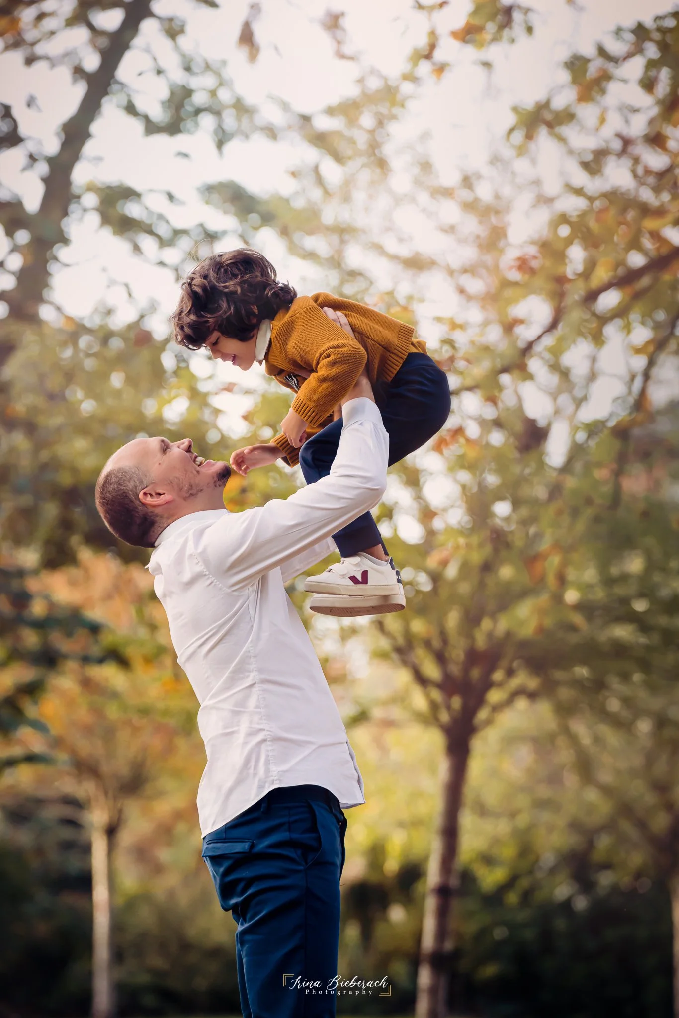 Papa lève son fils en l'air dans un parc parisien pendant un après-midi d'automne