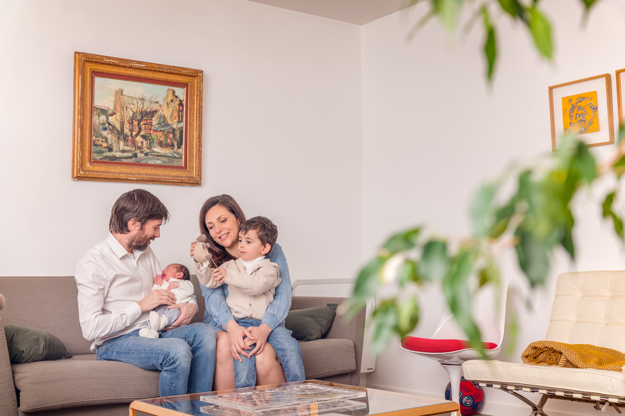 Famille dans un salon d’appartement parisien avec un bébé porté par son père et un petit garçon assis sur les genoux de sa maman