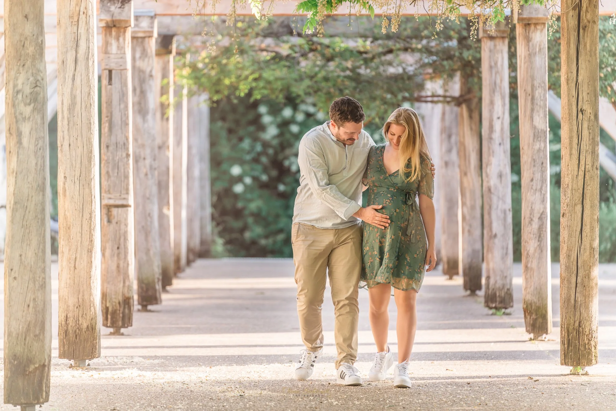 Couple de futurs parents font une balade dans une galerie naturelle, le futur père touche doucement le ventre rond de son épouse 
