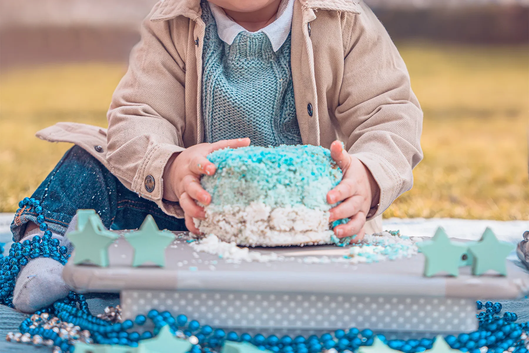 Bébé de 1 an avec les mains pleines de gâteau bleu, illustrant le besoin d'une tenue de rechange après un Smash the Cake.