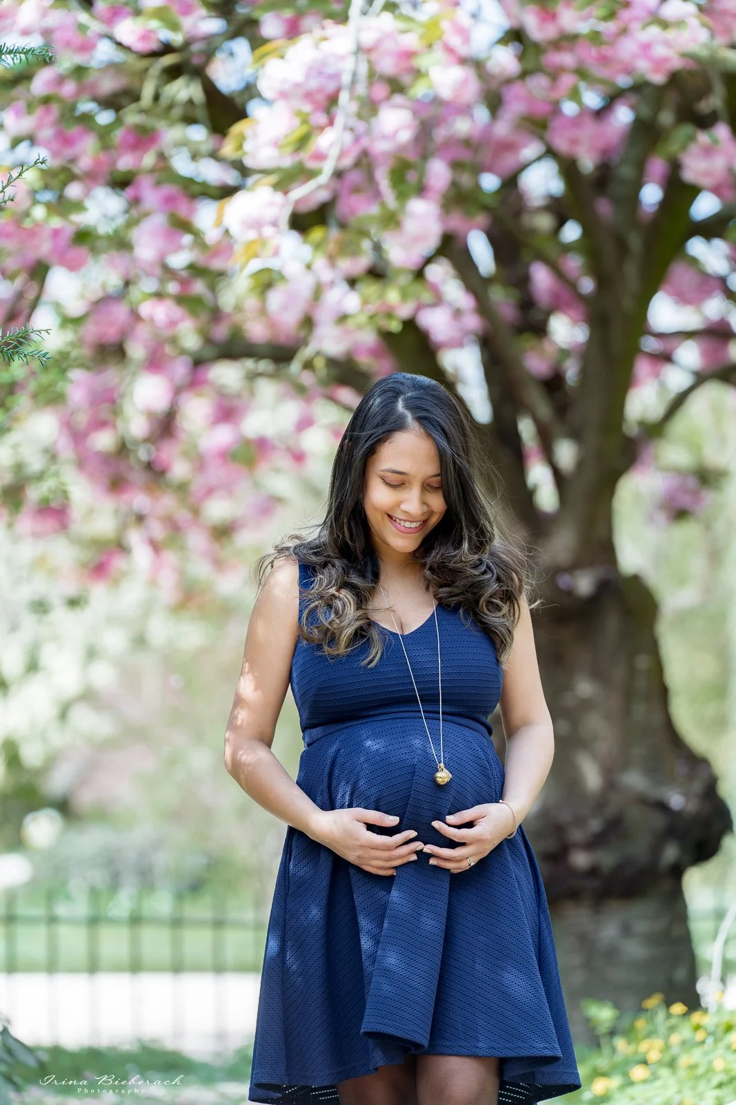 Jeune femme enceinte touche et regarde son ventre sous un cerisier en fleur