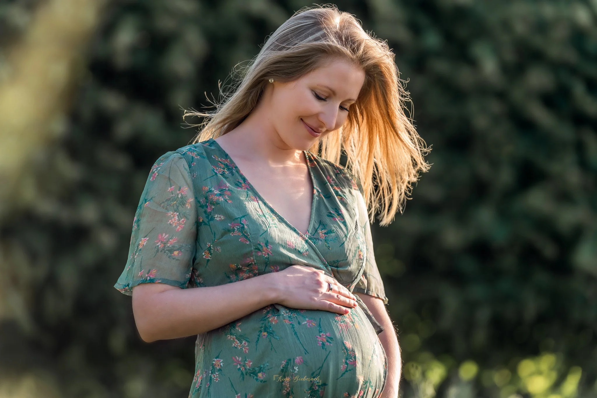 Femme blonde enceinte regarde et touche tendrement son ventre pendant un coucher de soleil dans le parc de l île Saint Germain