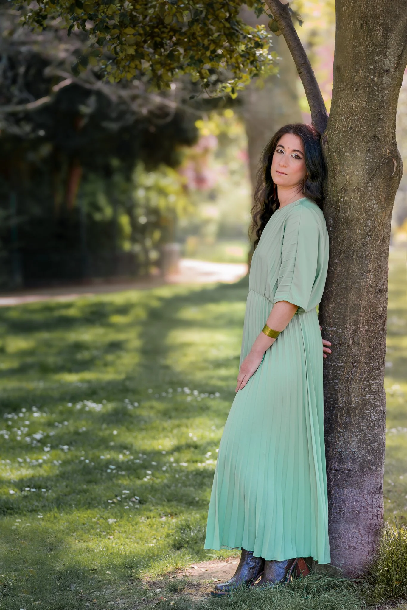 Portrait naturel de une femme brune en extérieur à Paris. Pose élégante contre un arbre sous la lumière d'un après-midi de printemps.