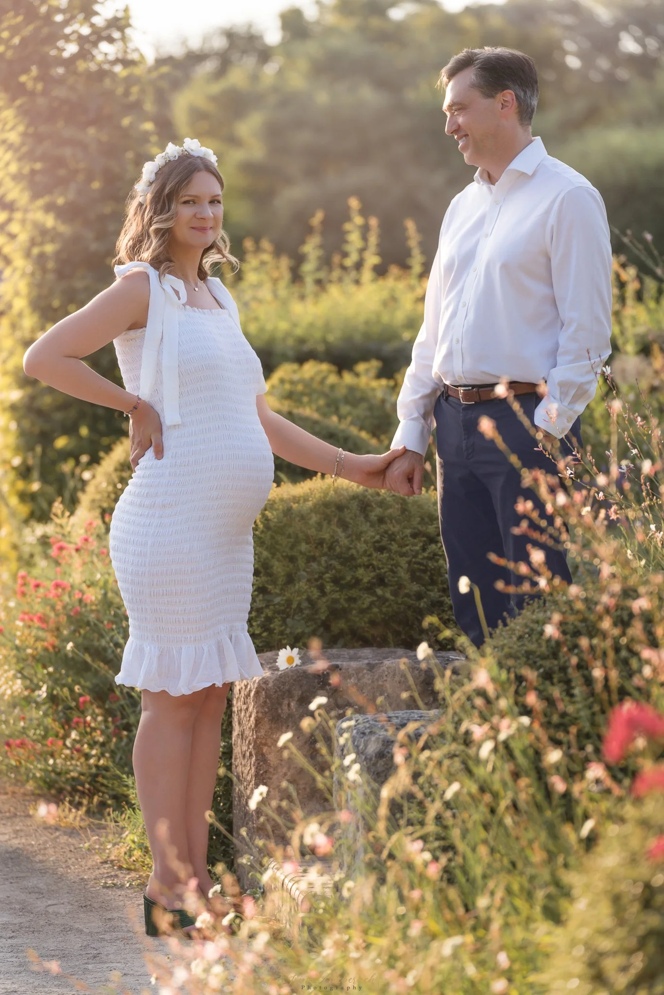 Femme enceinte prends la main de son époux qui sourit et la regarde pendant le coucher du soleil dans un parc aux alentours de Paris