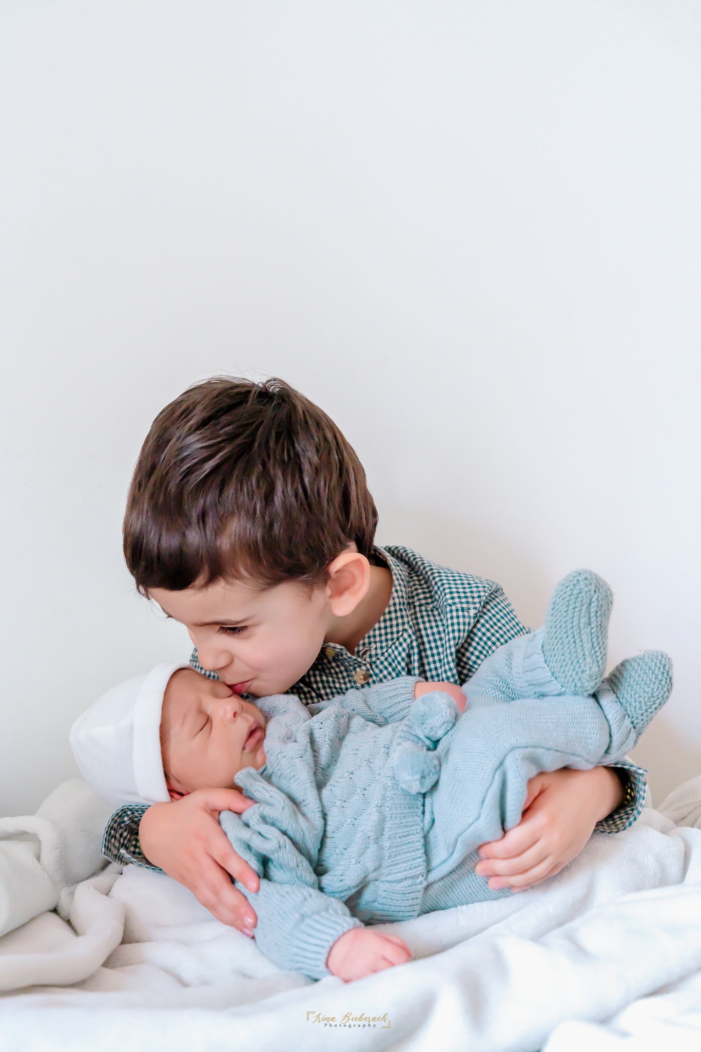 Petit garçon porte et embrasse doucement son frère nouveau né qui dort dans ses bras