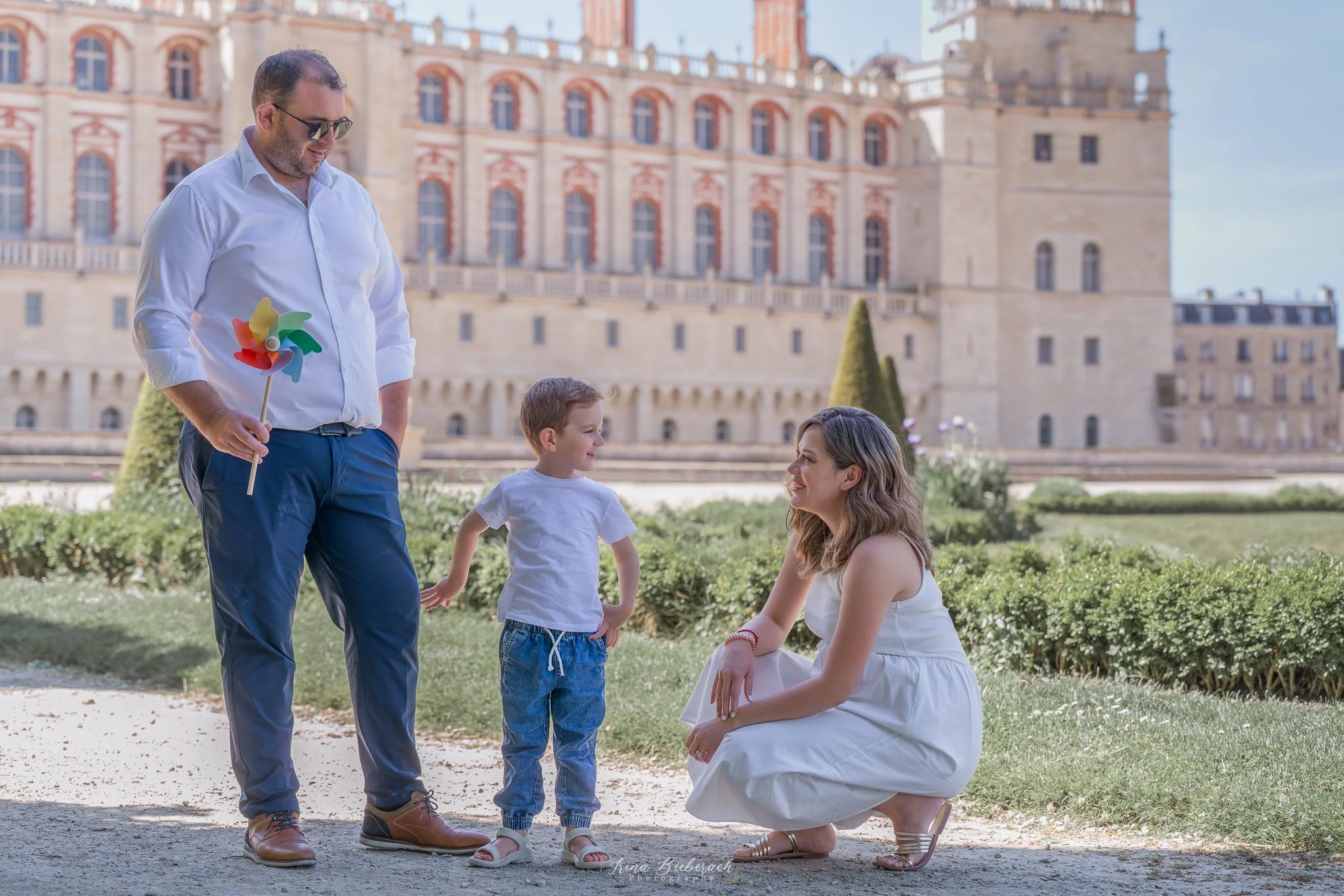 Femme enceinte parle avec son enfant devant le château de Saint Germain en Laye pendant que le mari les regarde en soutenant un petit moulin à vent coloré 