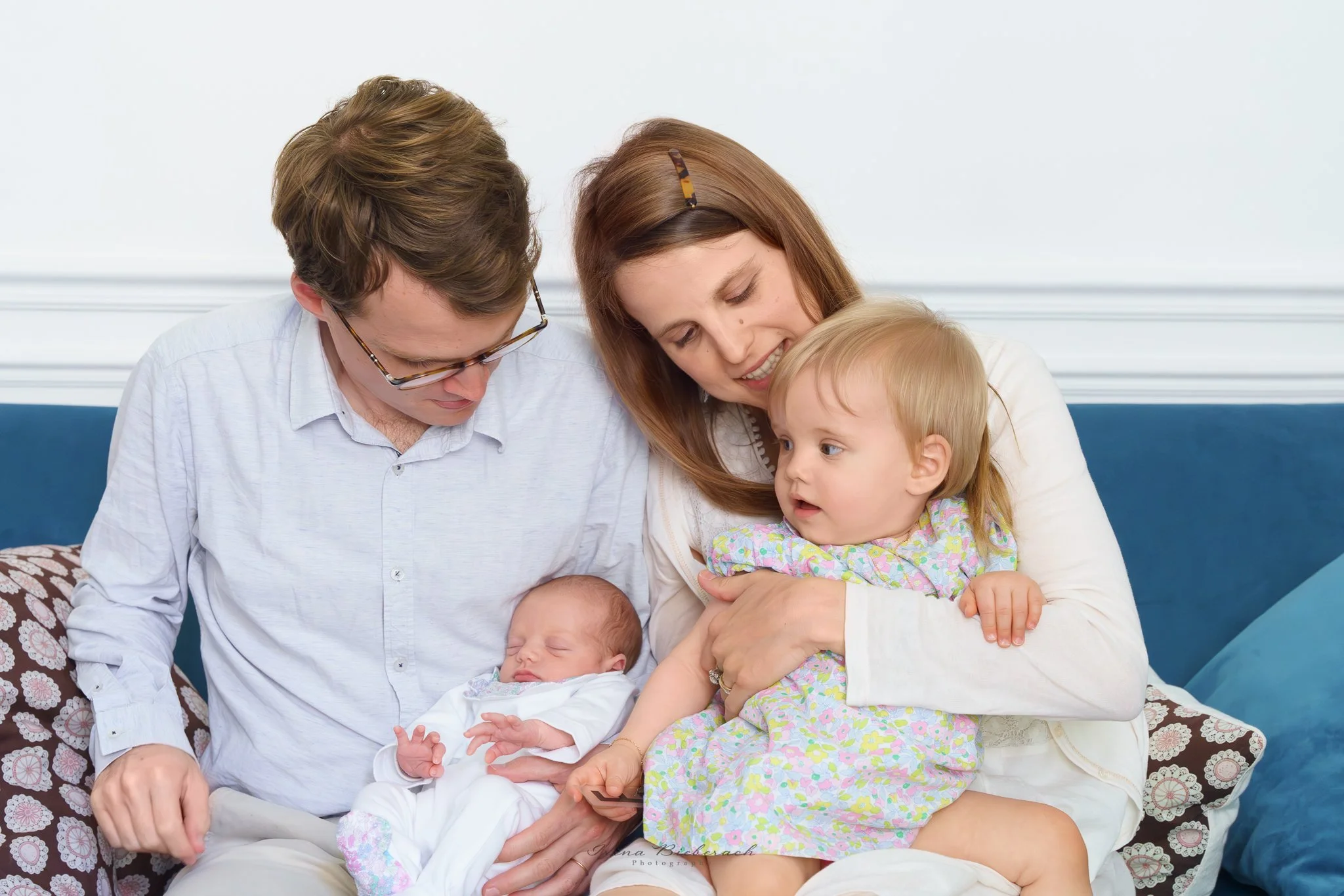 Famille de parents avec une bébé et un nourrisson assis sur un canapé bleu du salon de l’appartement parisien