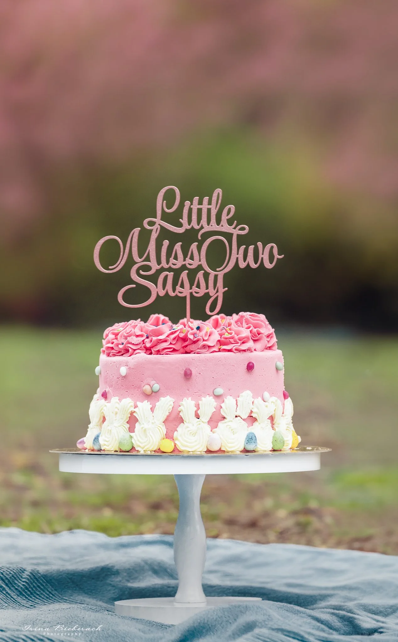 Gâteau d'anniversaire rose décorée lapins sur support en bois blanc et avec topper dans un parc