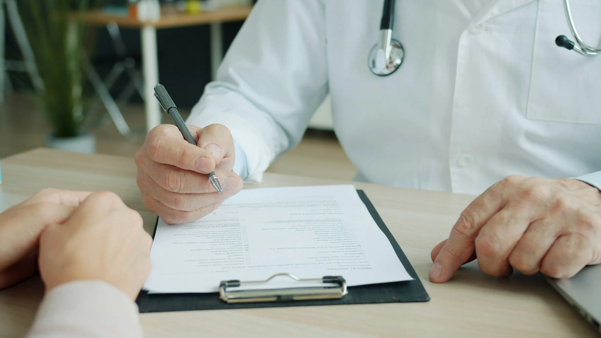Doctor in white coat signing a document for an elderly patient at a clinic or hospital desk.