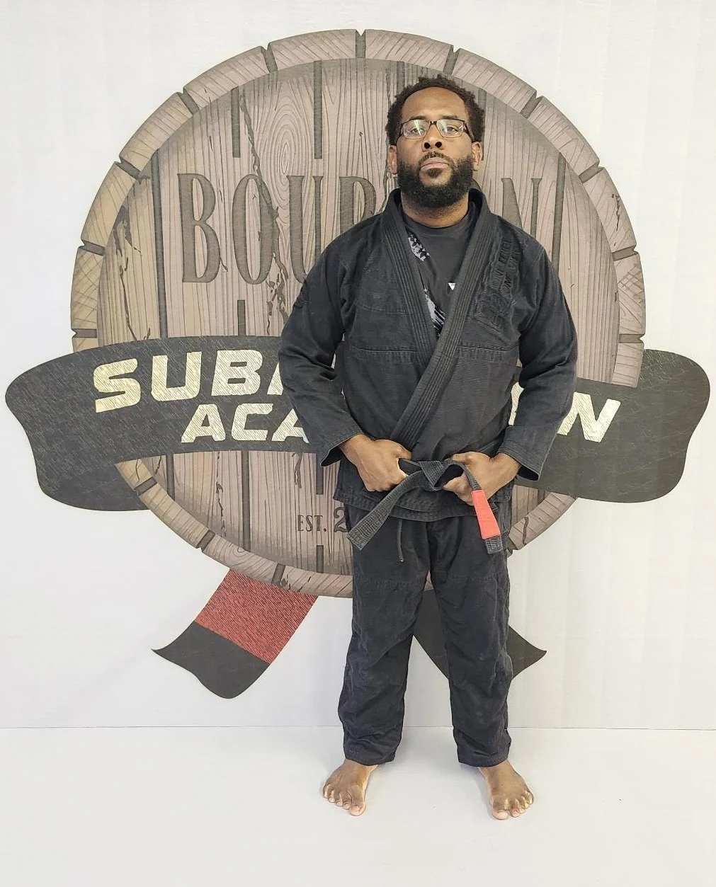 Two men practicing Brazilian Jiu-Jitsu on an outdoor mat, wearing gis, with other people training in the background.