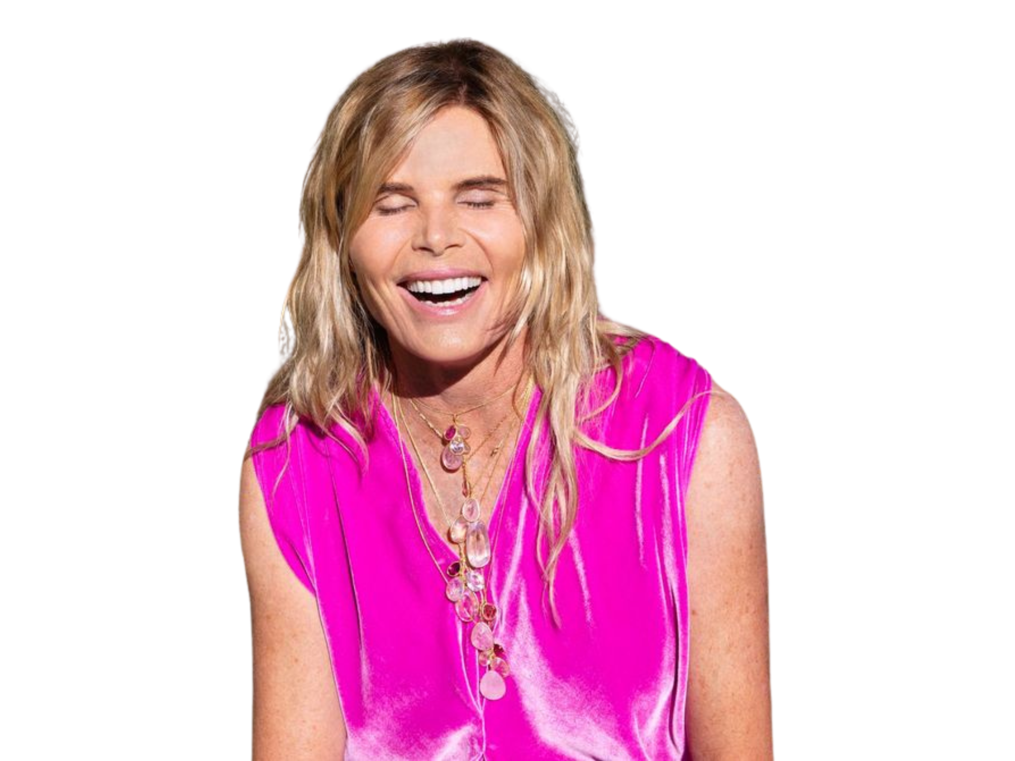 A woman with blonde wavy hair wearing a bright pink sleeveless top and layered necklaces, smiling with her eyes closed.