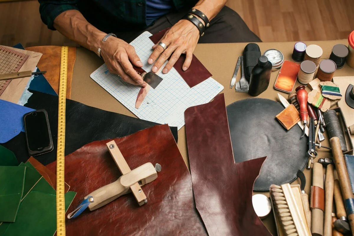 Un artisan en train de couper du cuir avec des outils et des échantillons de cuir autour de lui.