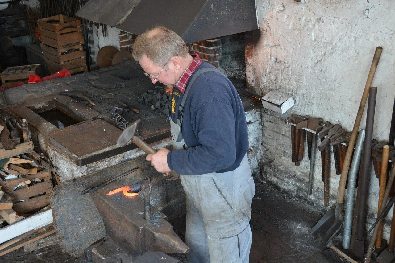 Artisan forger travaillant dans un atelier de forge traditionnel avec un marteau et un feu de forge.