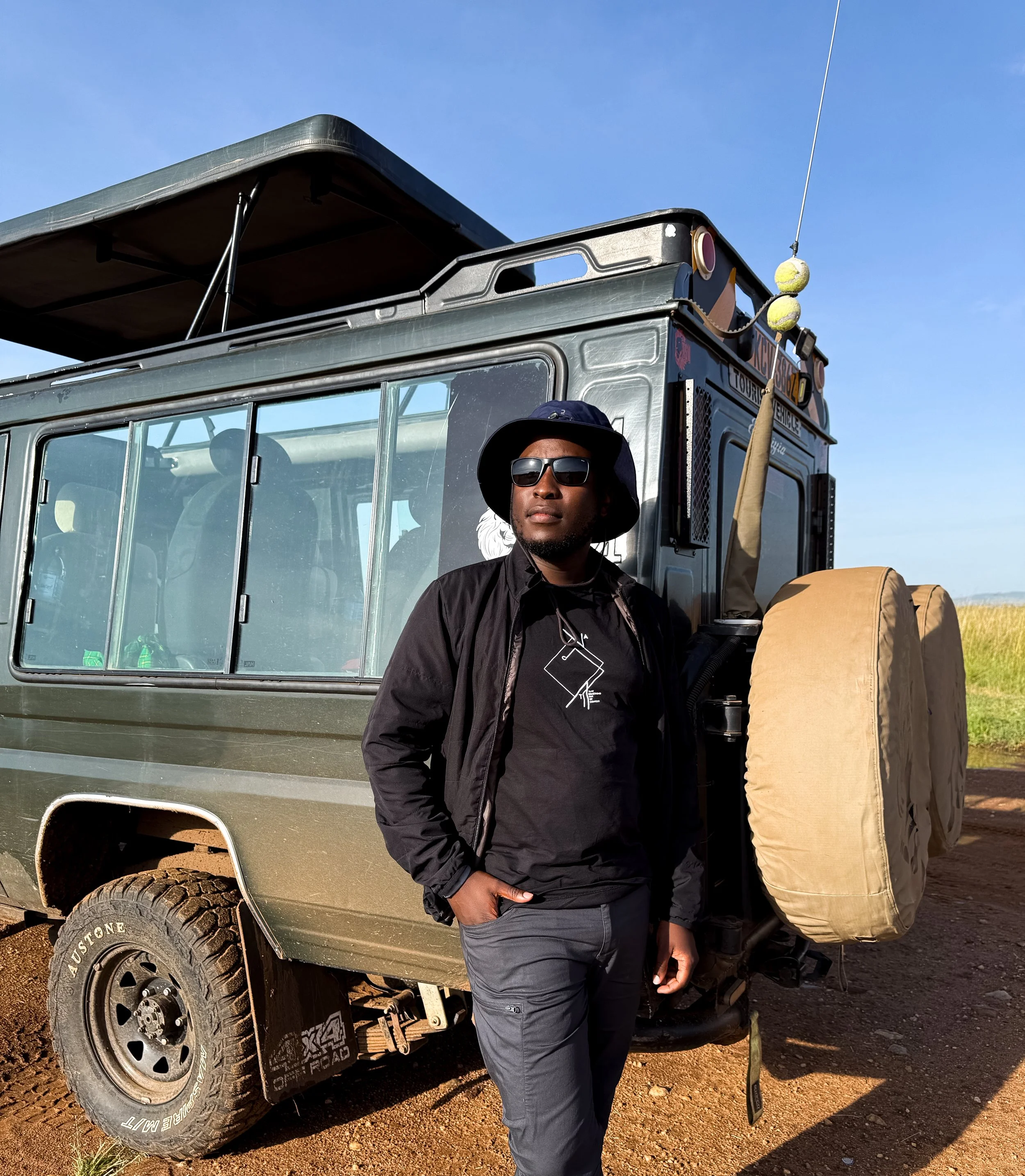 A man with sunglasses and a black hat standing next to a modified off-road vehicle in a rural outdoor setting.