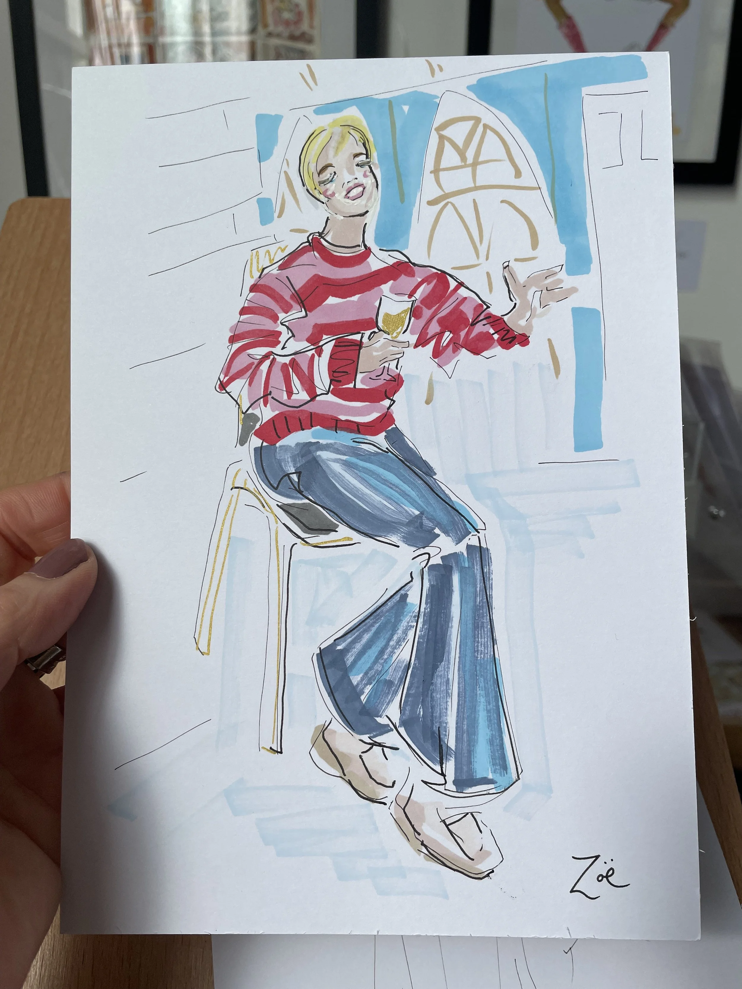 A colorful sketch of a young woman with short blonde hair sitting on a chair, wearing a red and pink striped sweater and blue jeans, holding a glass of white wine with a gold emble in a cozy indoor setting with large windows in the background.