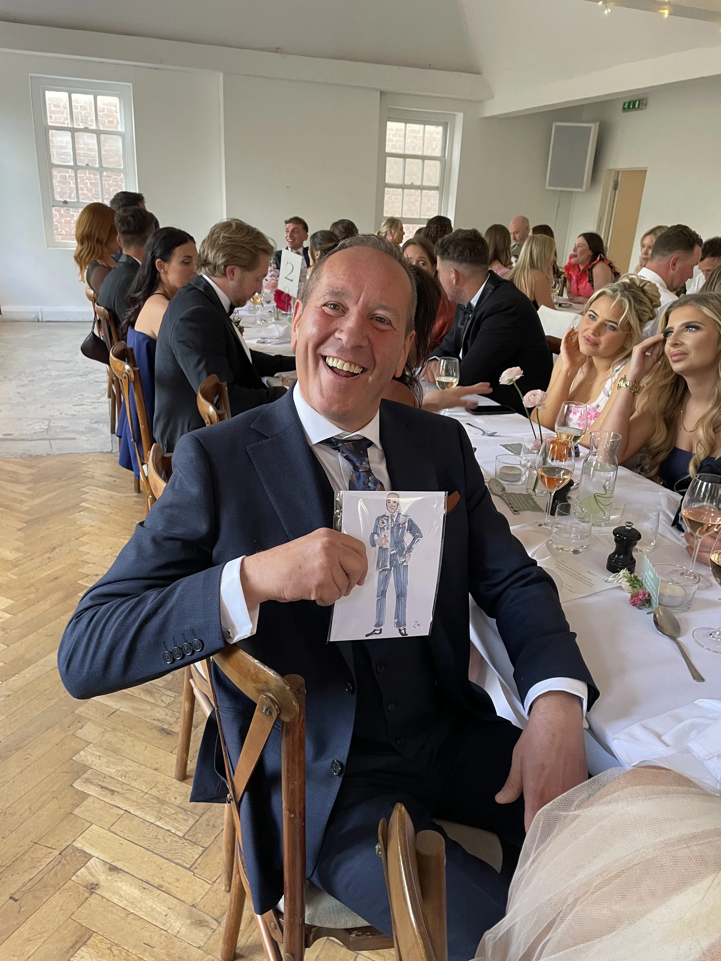 Photo of father of the bride at a wedding reception looking really happy with a live wedding illustration by Zoe Parker Illustration. He is sitting at a long table with all the guests.