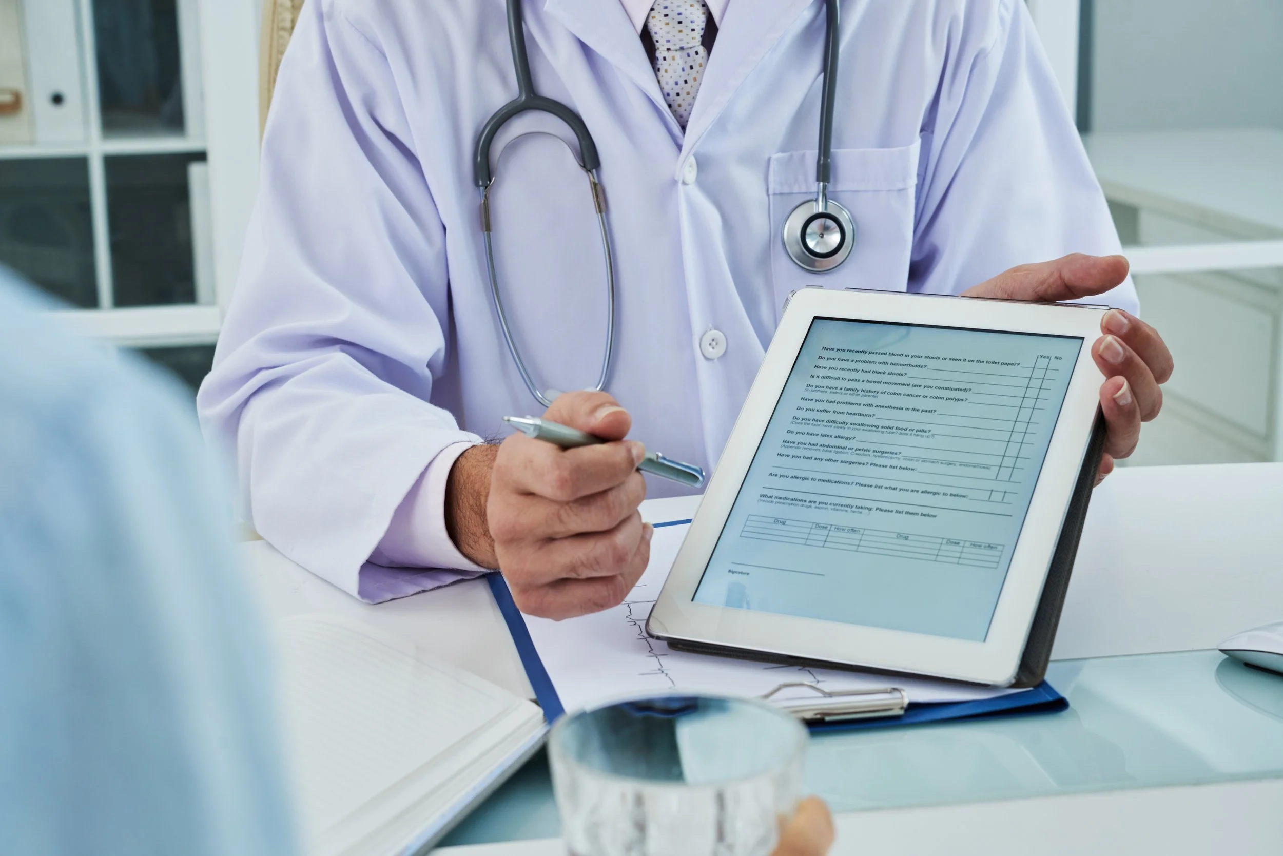 Doctor showing a patient a digital medical form on a tablet in a clinic or hospital setting.