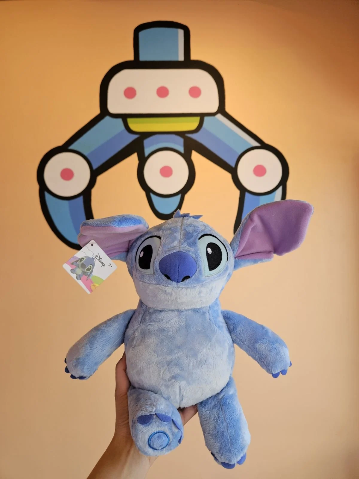 A plush toy of Stitch from Disney's Lilo & Stitch being held in front of the Orange Claw Club mural in Downtown Santa Ana.