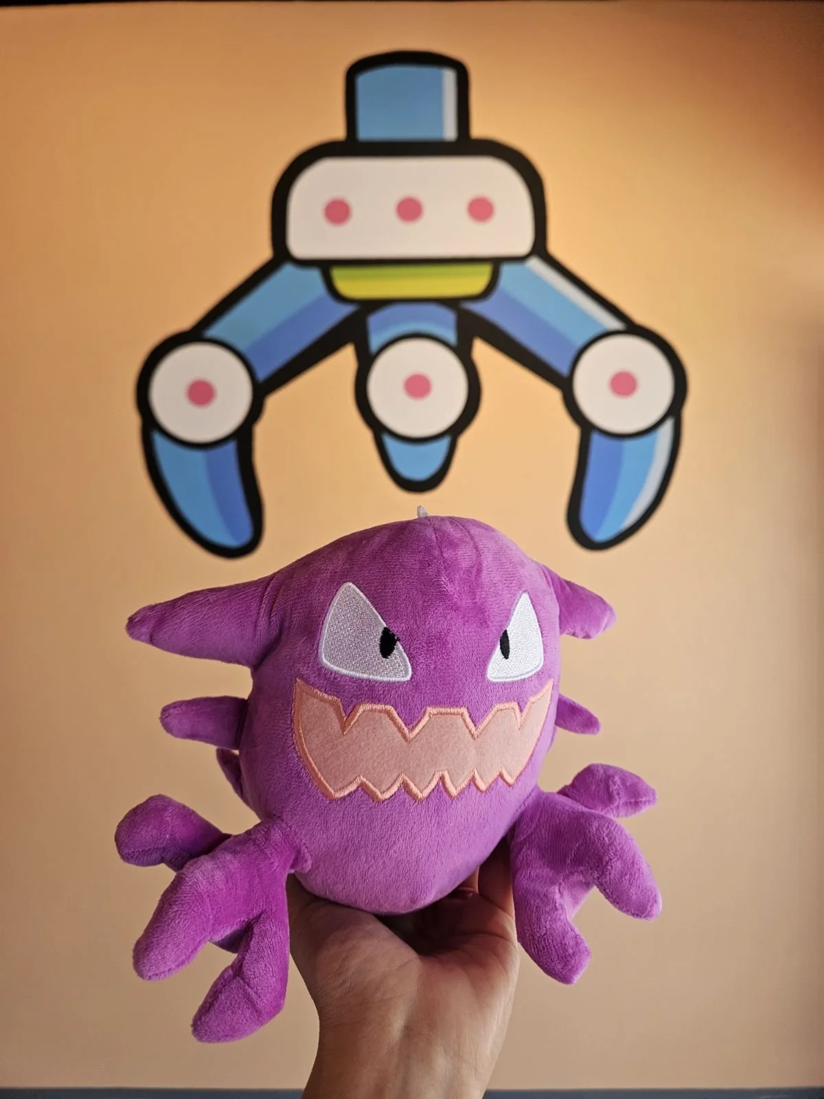 Purple Haunter Pokemon plush toy with multiple limbs held in front of the Orange Claw Club mural in Downtown Santa Ana.