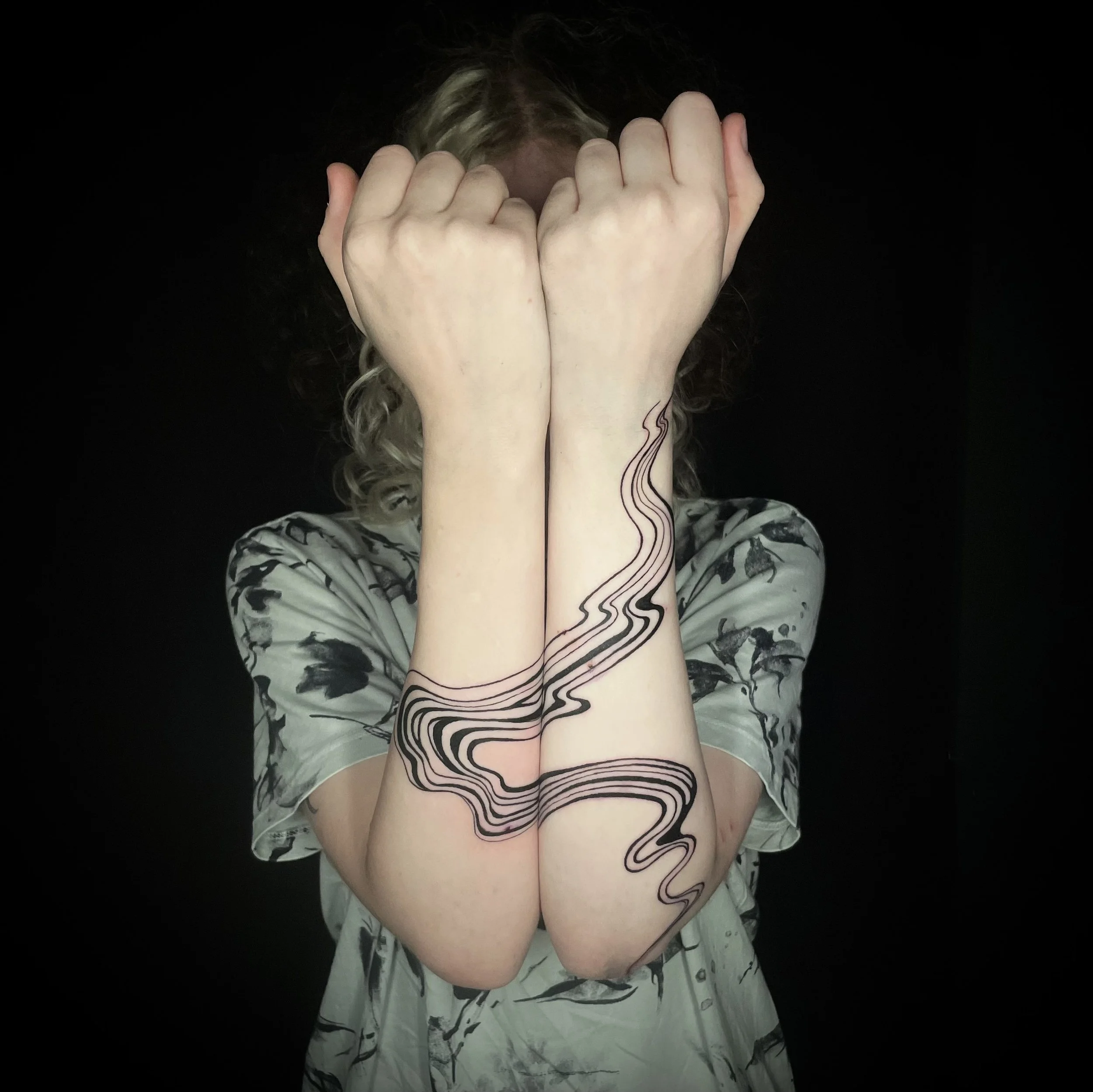 Tatouage de Wootz aux lignes noires ondulées, formant un motif continu lorsque les deux avant-bras sont rapprochés.