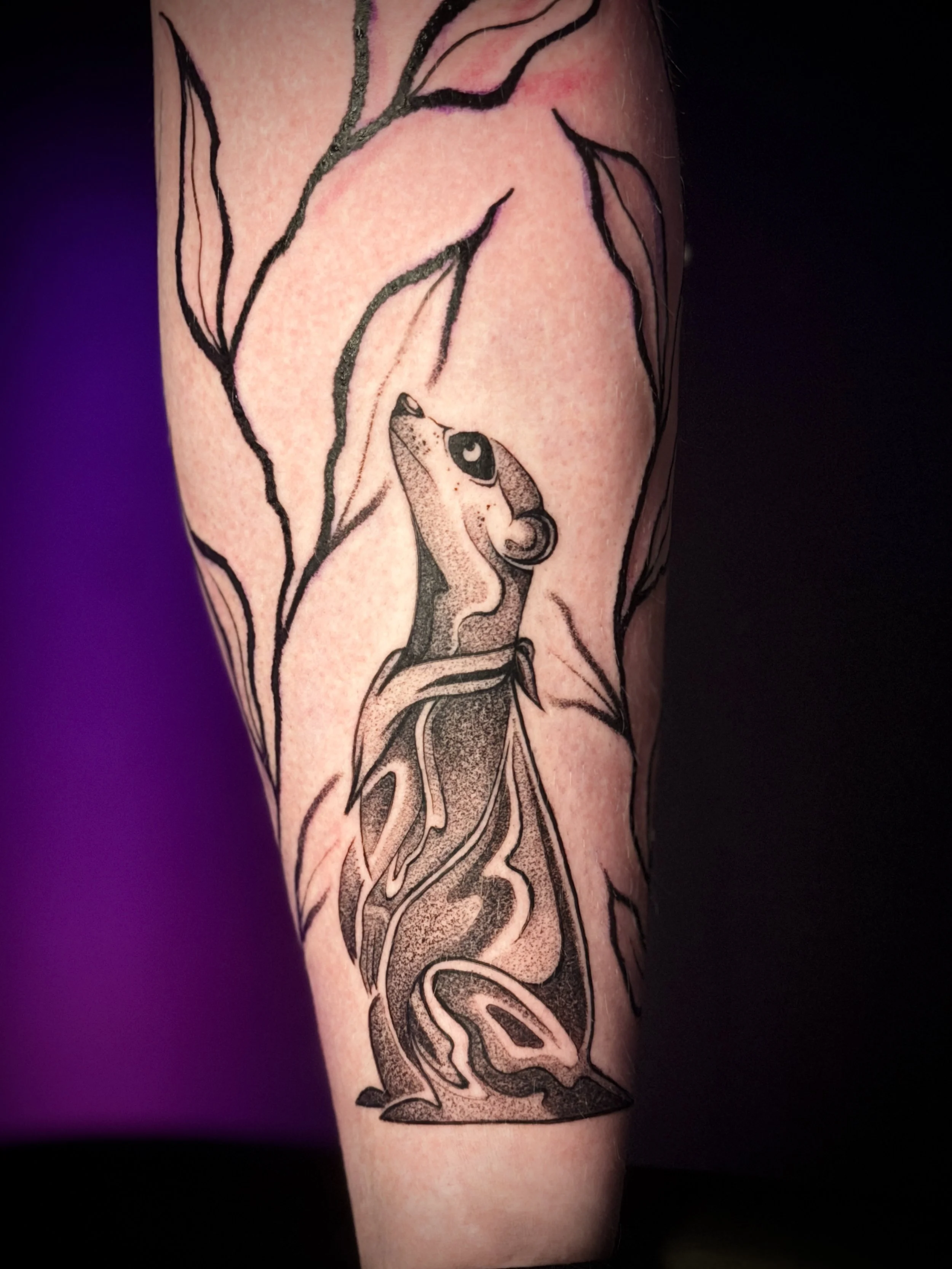 Tatouage de Wootz représentant un petit mammifère dressé parmi des branches feuillues, avec des motifs noirs et des ombrages en pointillés.