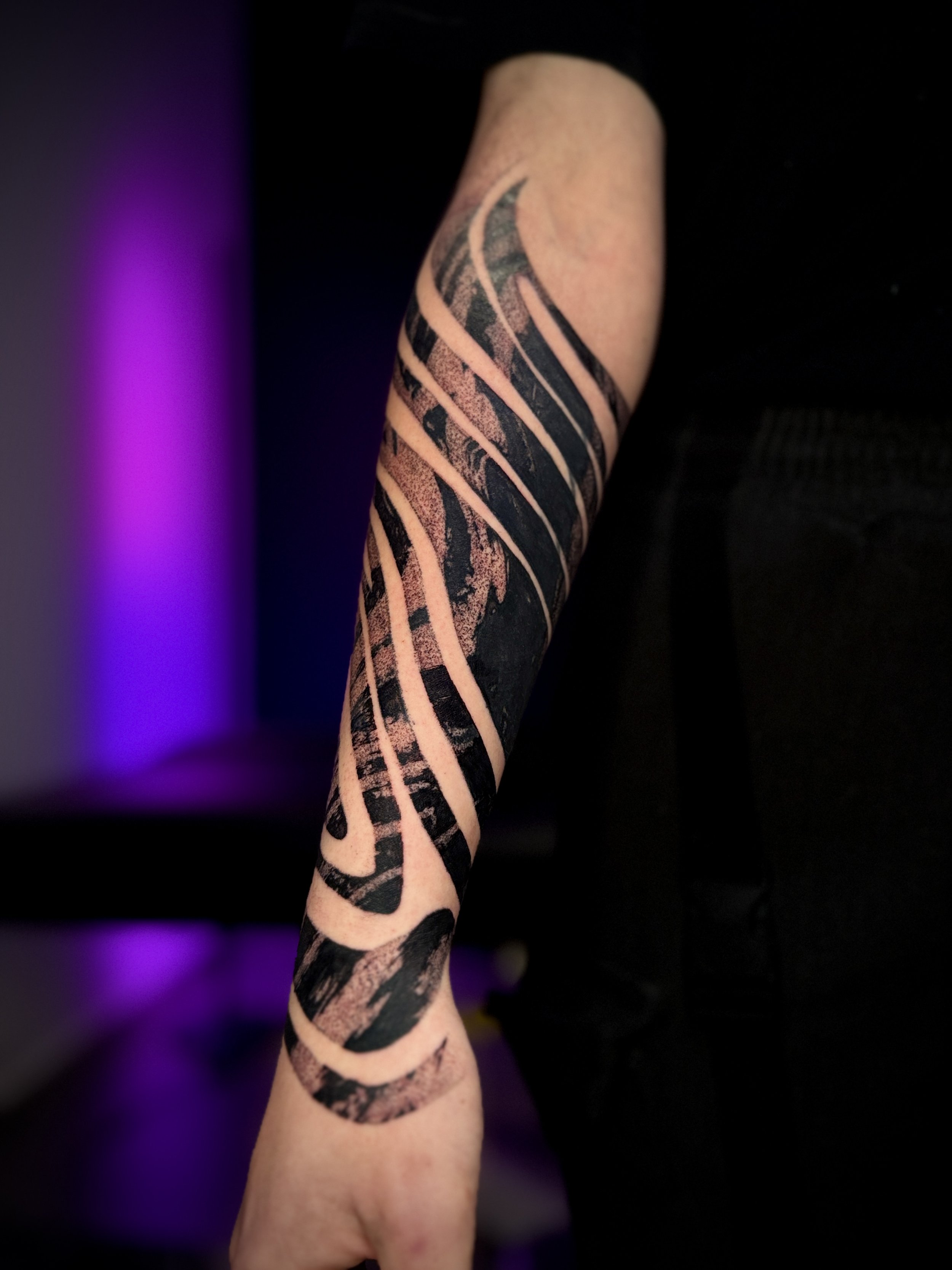 Tatouage abstrait recouvrement cover de Wootz sur l’avant-bras, composé de bandes noires courbes et texturées, séparées par des espaces de peau.