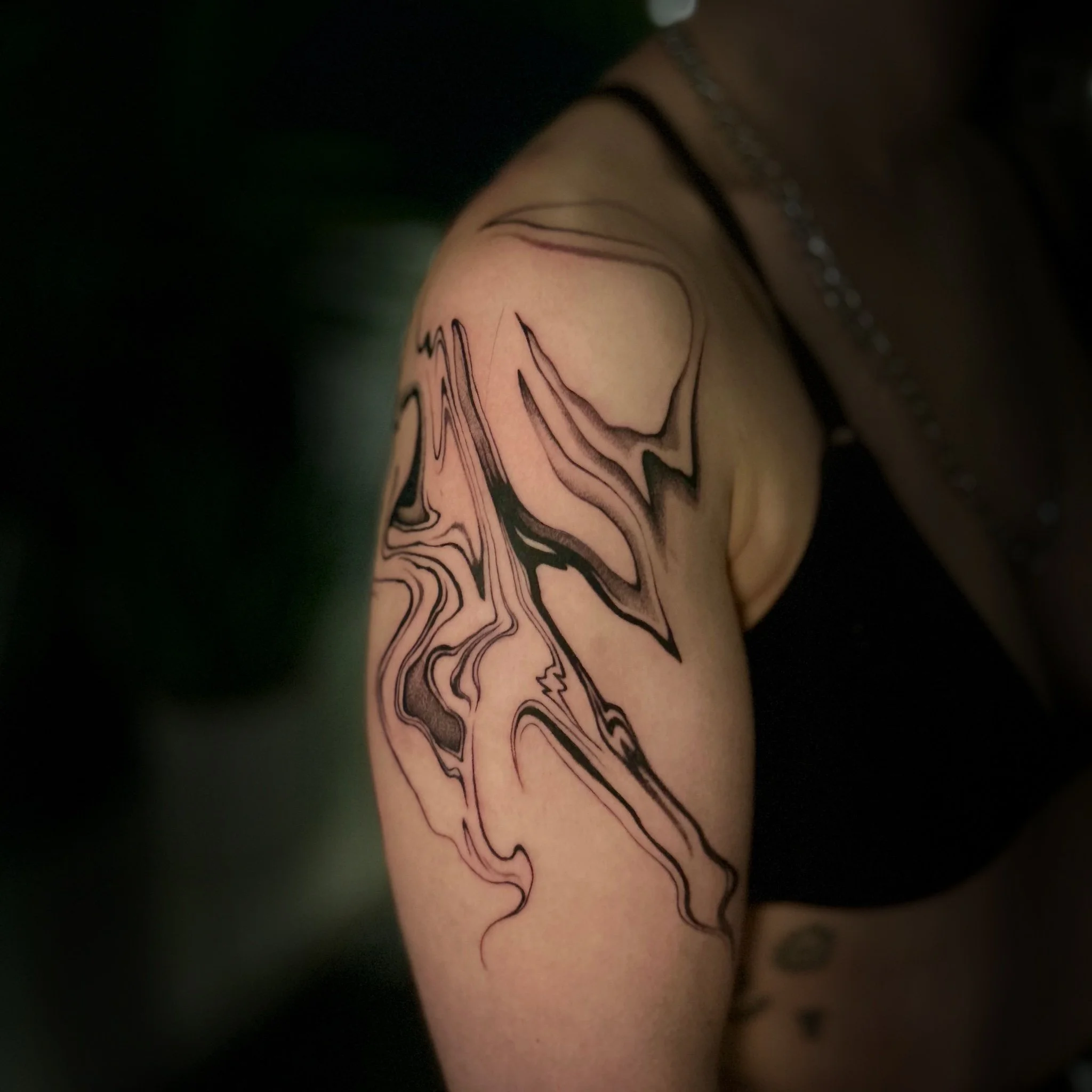 Tatouage abstrait de Wootz sur l’épaule et le haut du bras, mêlant courbes fluides, pointes effilées et ombrages noirs et gris.