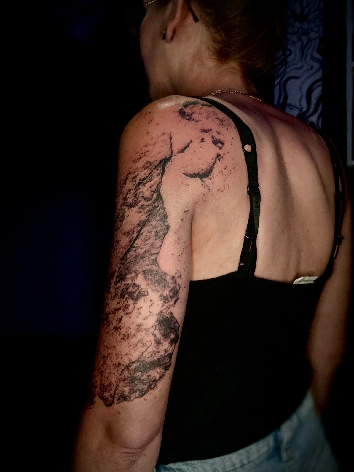 Tatouage abstrait de Wootz s’étendant de l’épaule au coude, composé de textures noires et grises aux contours irréguliers.