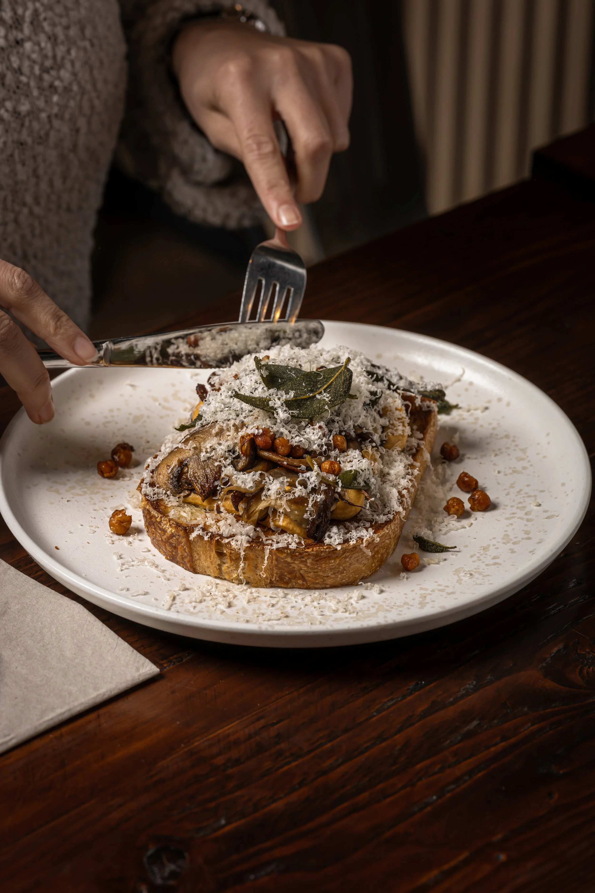 A plate of toasted bread topped with sautéed mushrooms, herbs, grated cheese, and garnished with a bay leaf, on a wooden table.